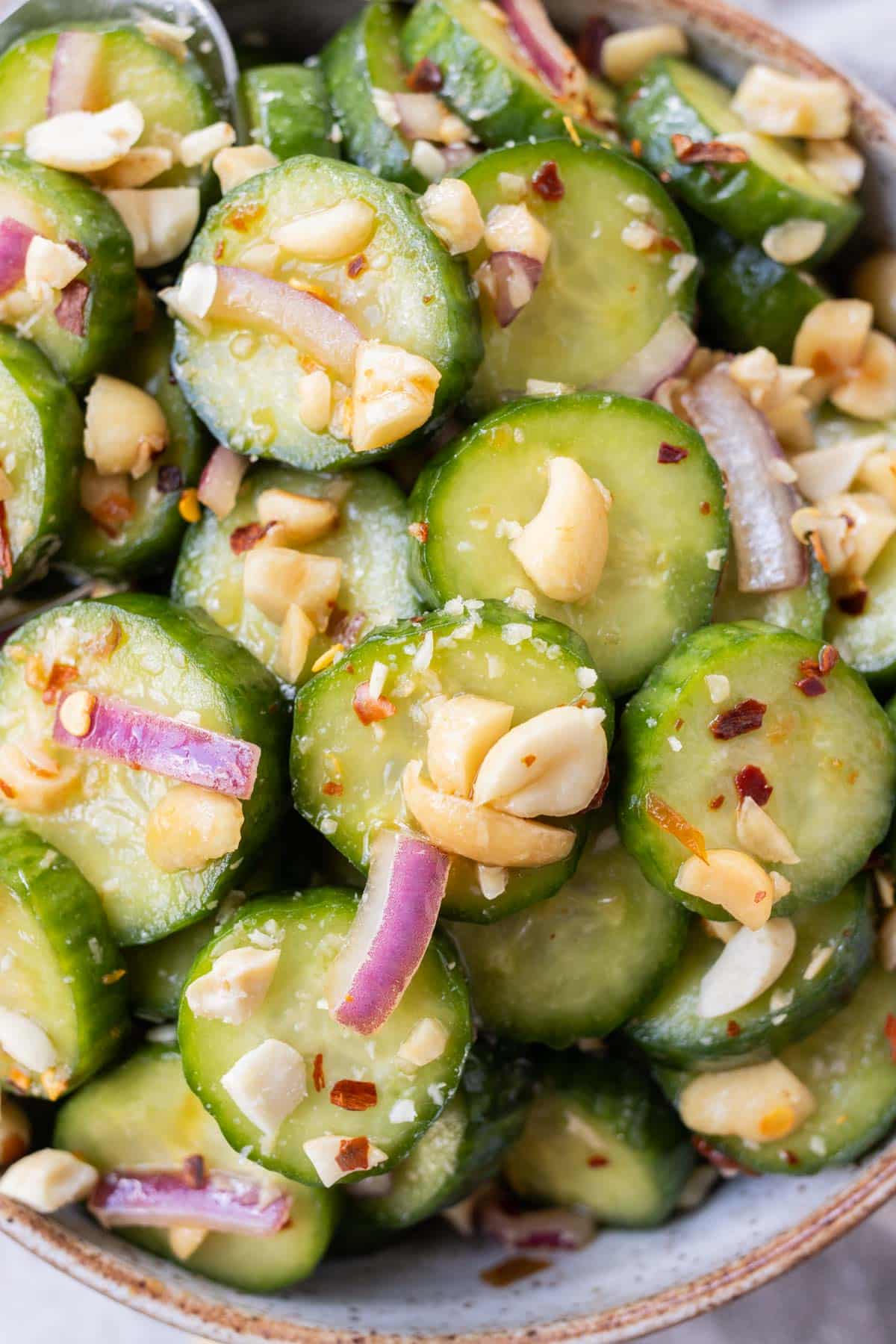 A spicy Asian cucumber salad with nuts in a white bowl.