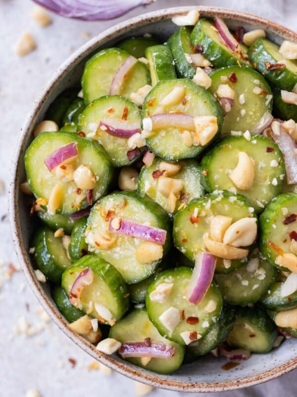 A spicy Asian cucumber salad with crushed peanuts and red onion in a serving bowl.