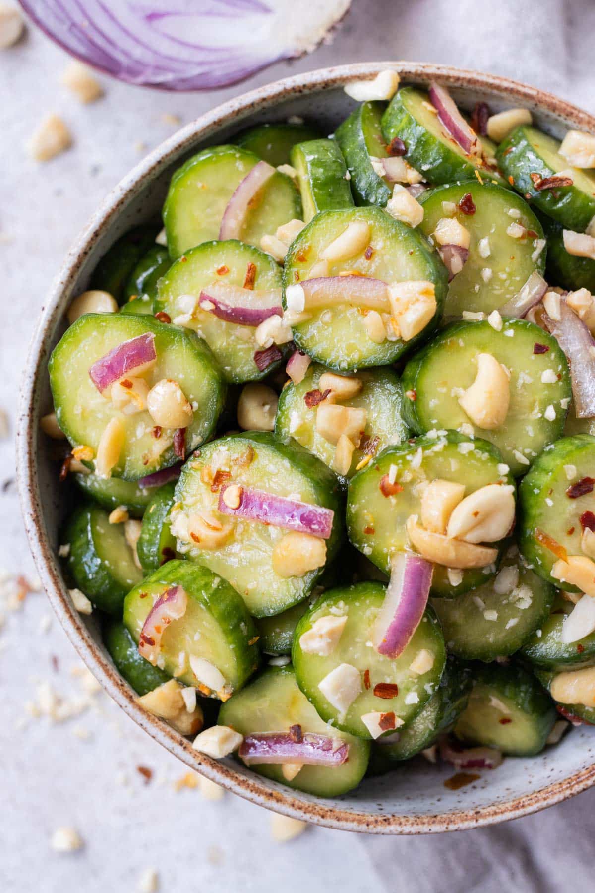 A spicy Asian cucumber salad with crushed peanuts and red onion in a serving bowl.