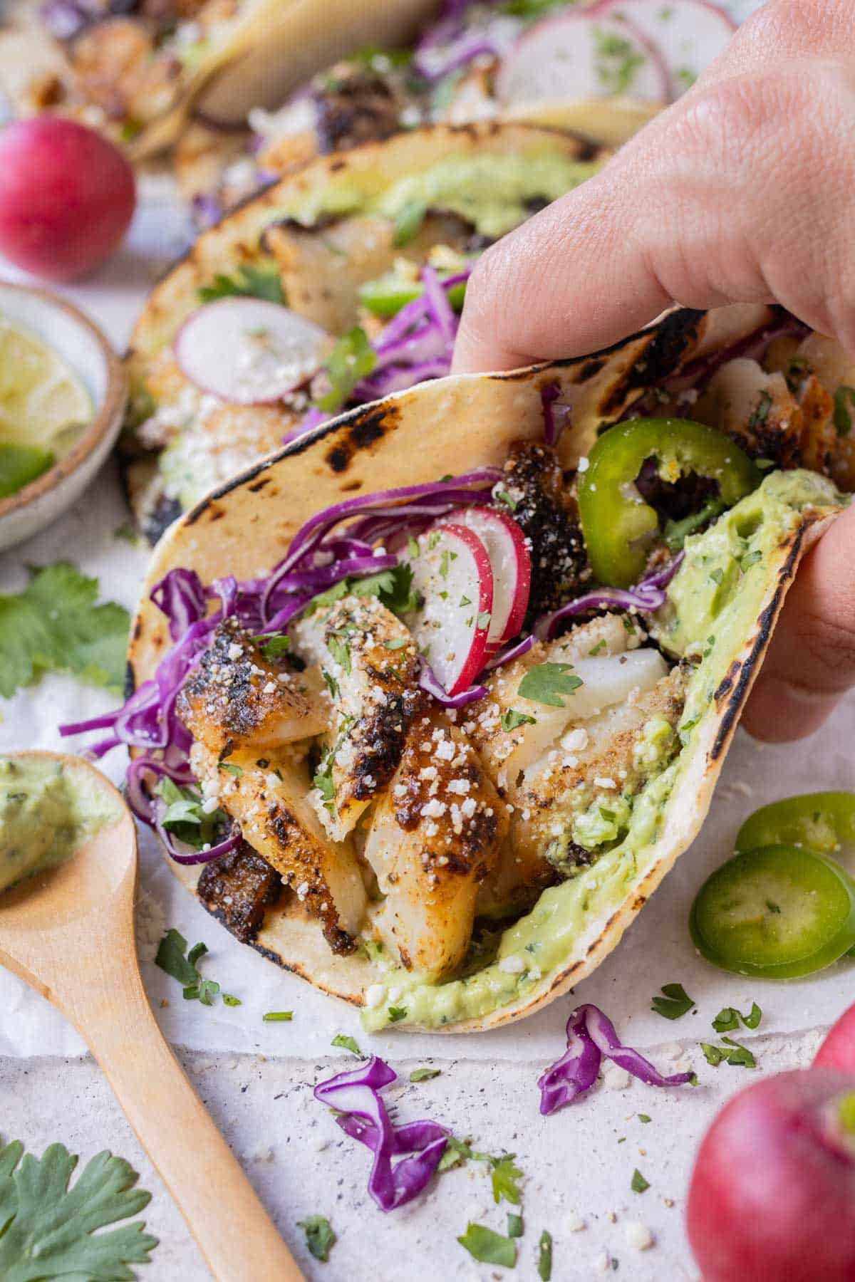 A pair of hands picking up a gluten-free Blackened Fish Taco for a healthy lunch.