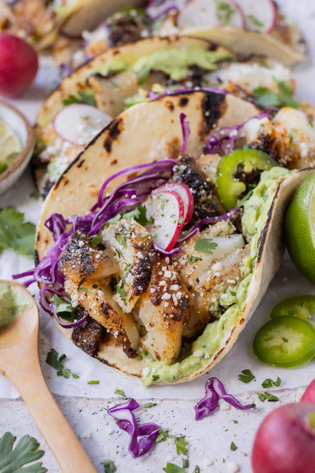 A blackened fish taco recipe that is served with a homemade avocado sauce and topped with shredded cabbage.