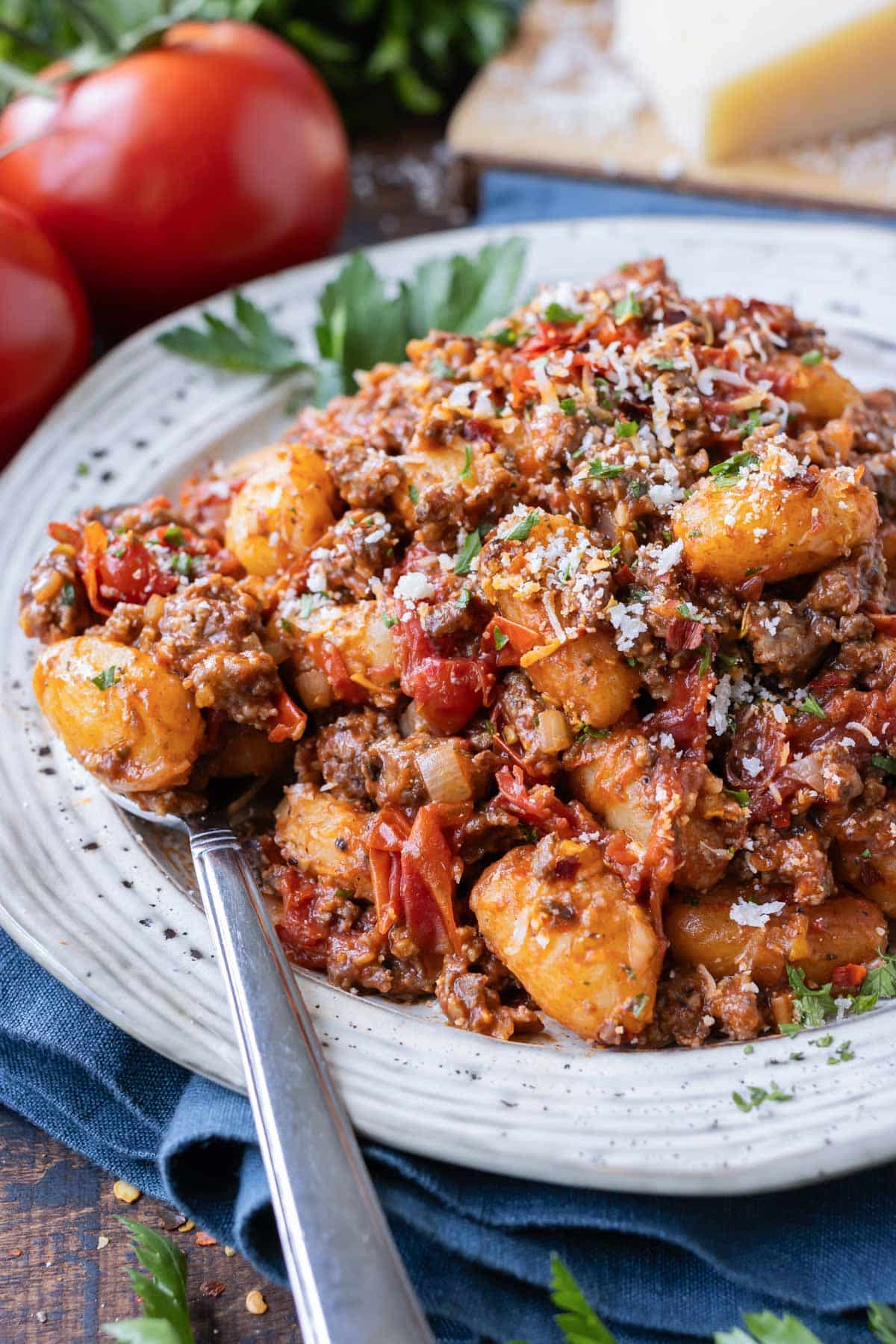 Gnocchi beef bolognese is served on a plate with a spoon and topped with Parmesan cheese.