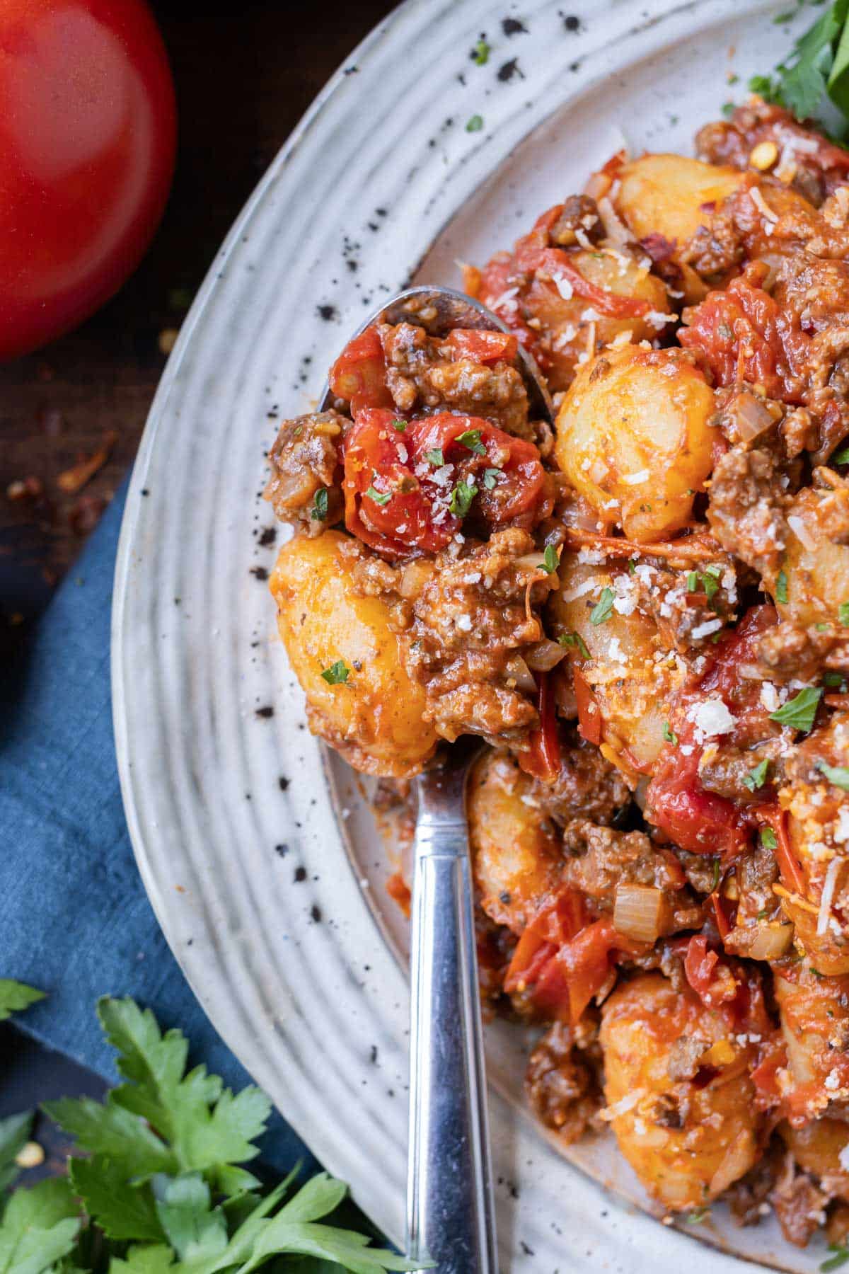 A fork digs into a white bowl with gnocchi Bolognese.