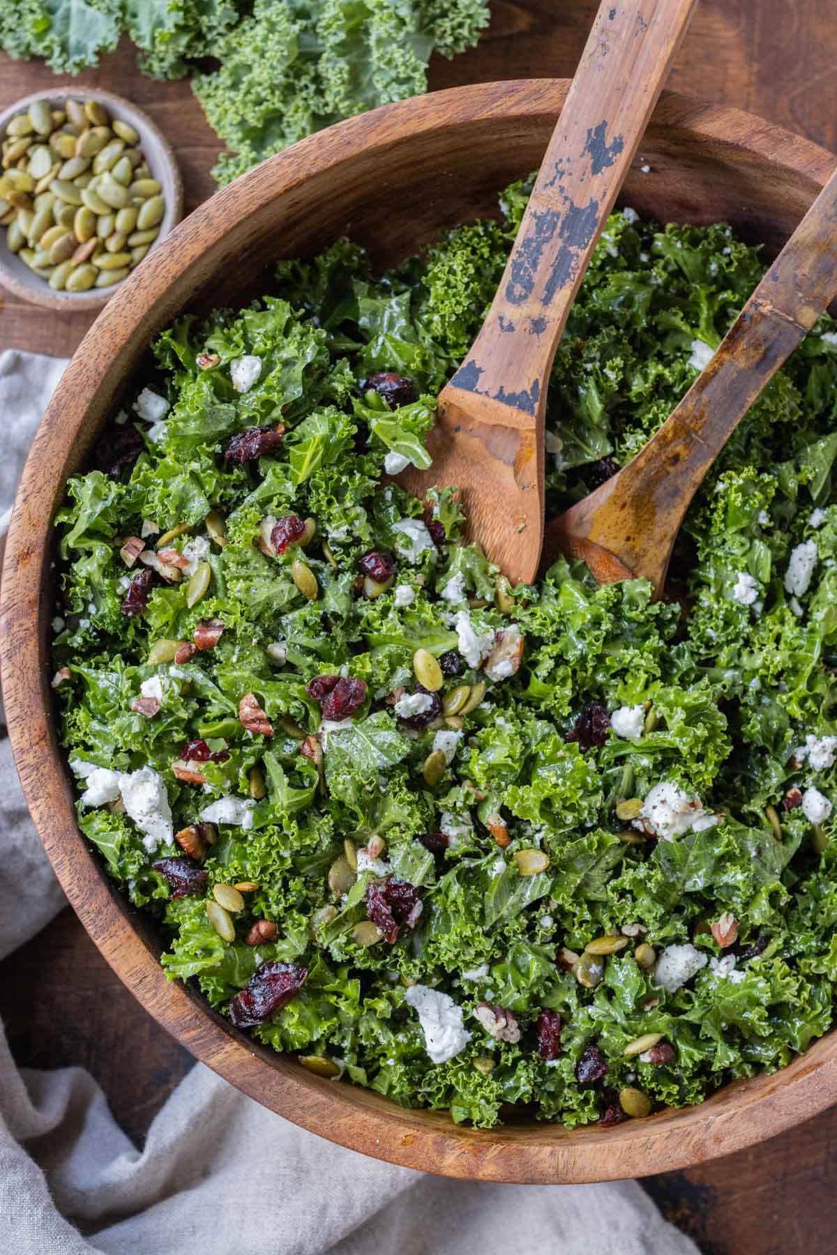 A wooden bowl is full of a chopped kale salad with cranberries.