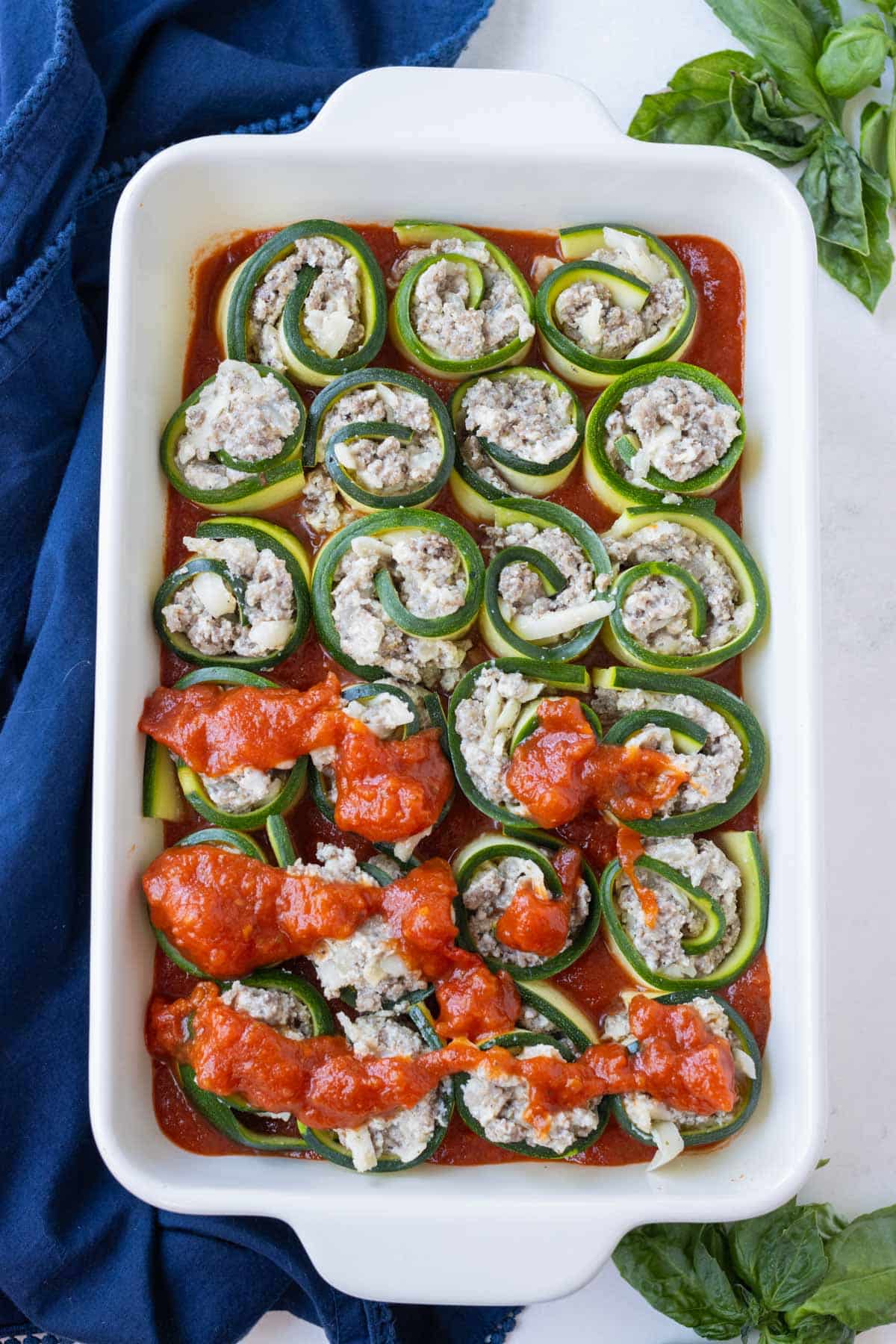 Rolled zucchini lasagna pieces are covered with red sauce.