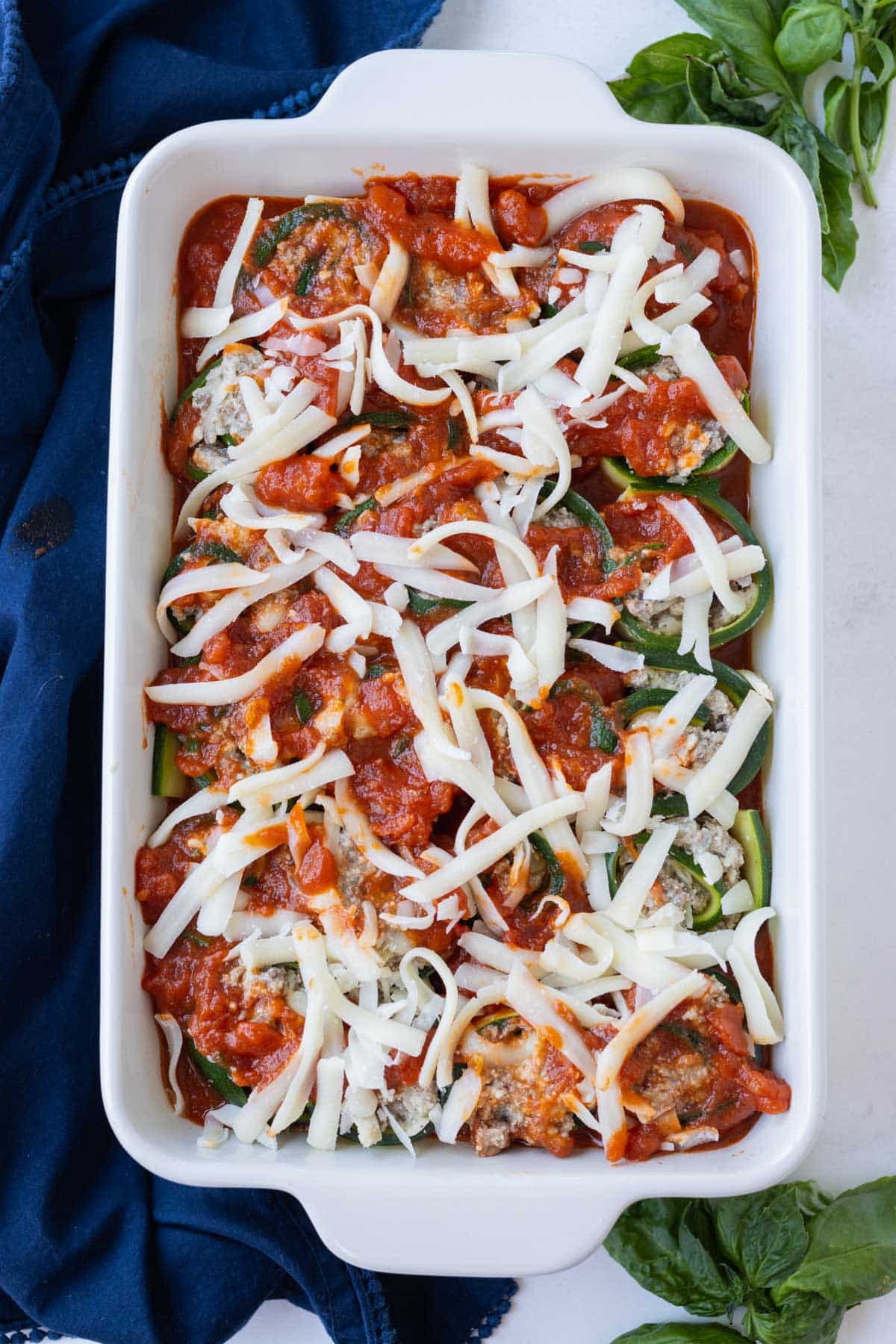 Cheese is sprinkled on top of the rolled zucchini lasagna.