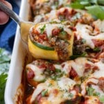 A zucchini lasagna roll-up being pulled from a baking dish with a fork.