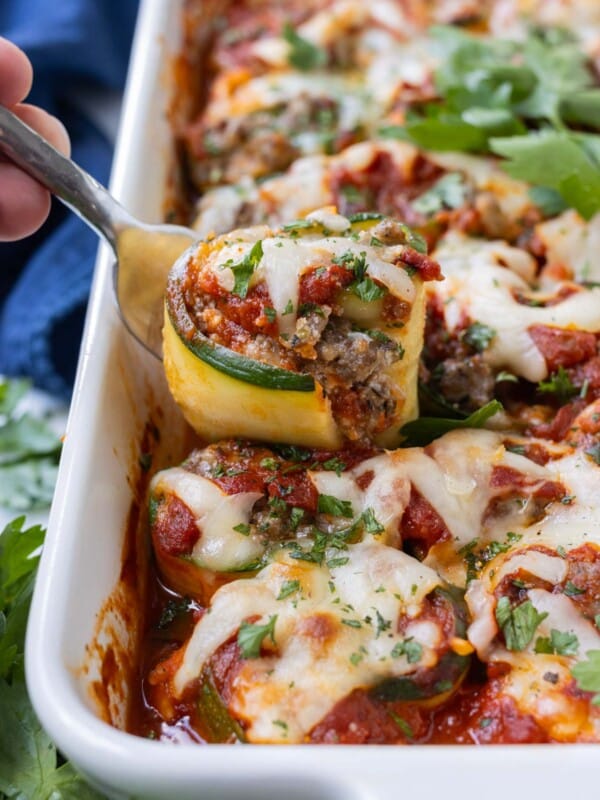 A zucchini lasagna roll-up being pulled from a baking dish with a fork.