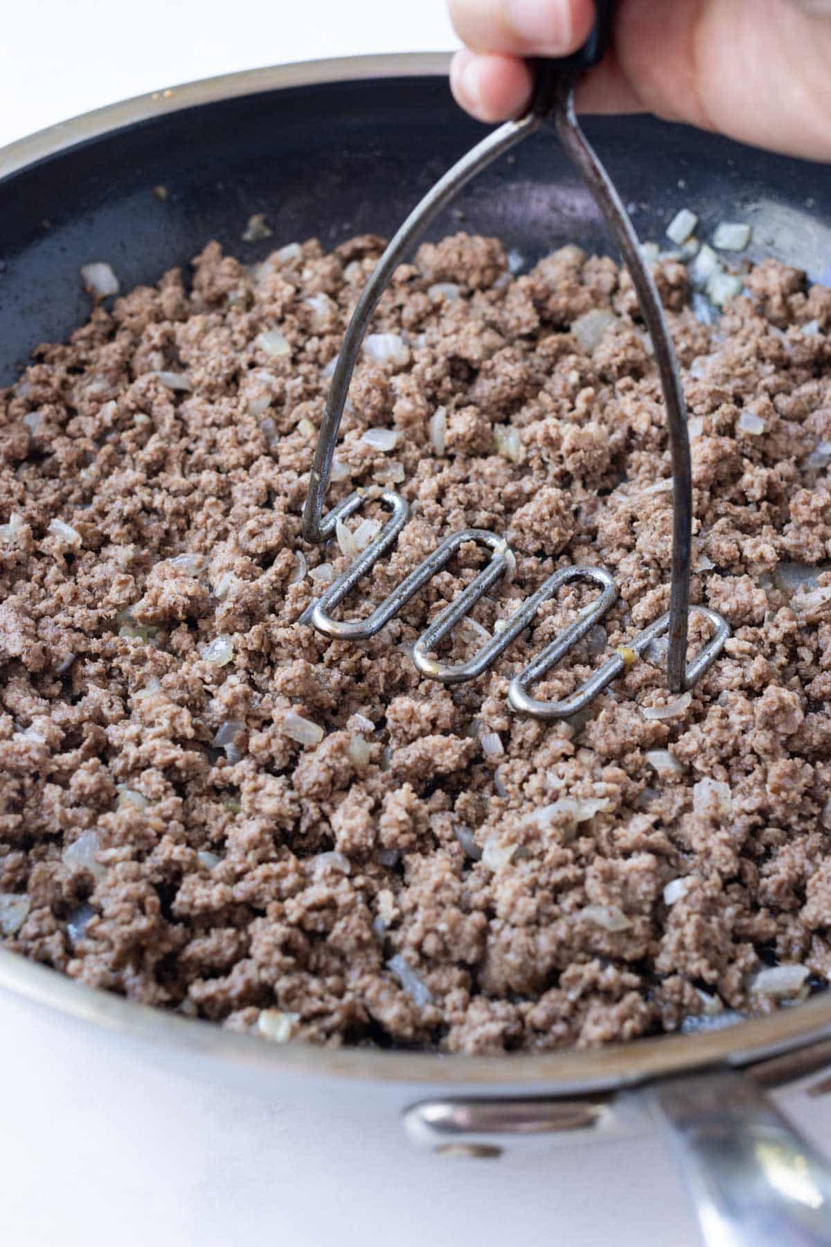 Ground meat is cooked and crumbled in a pan.