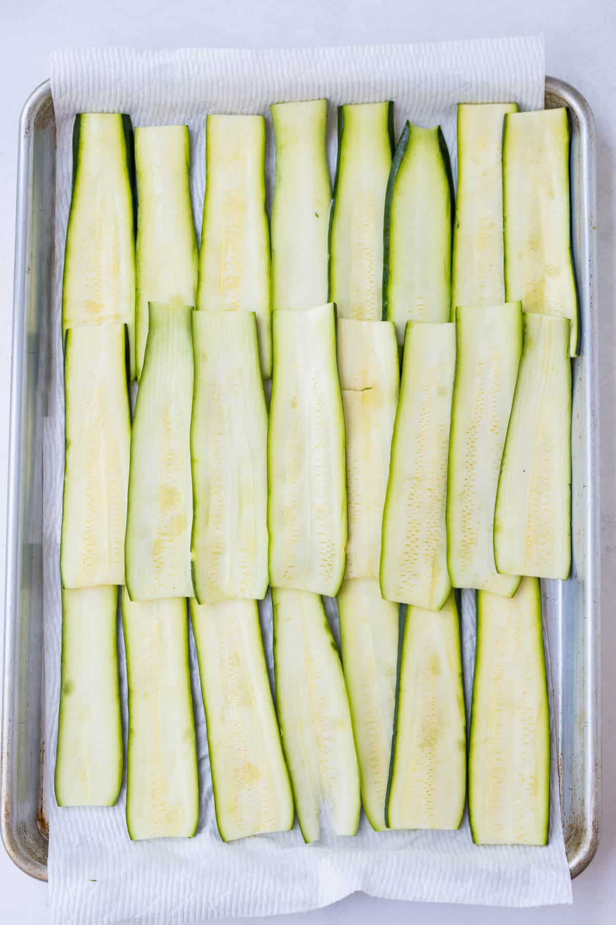 Zucchini strips are spread out and sprinkled with salt.