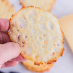 A hand holds a baked Parmesan crisp.