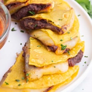 A tray of corn tortilla quesadillas are served on a tray with salsa.