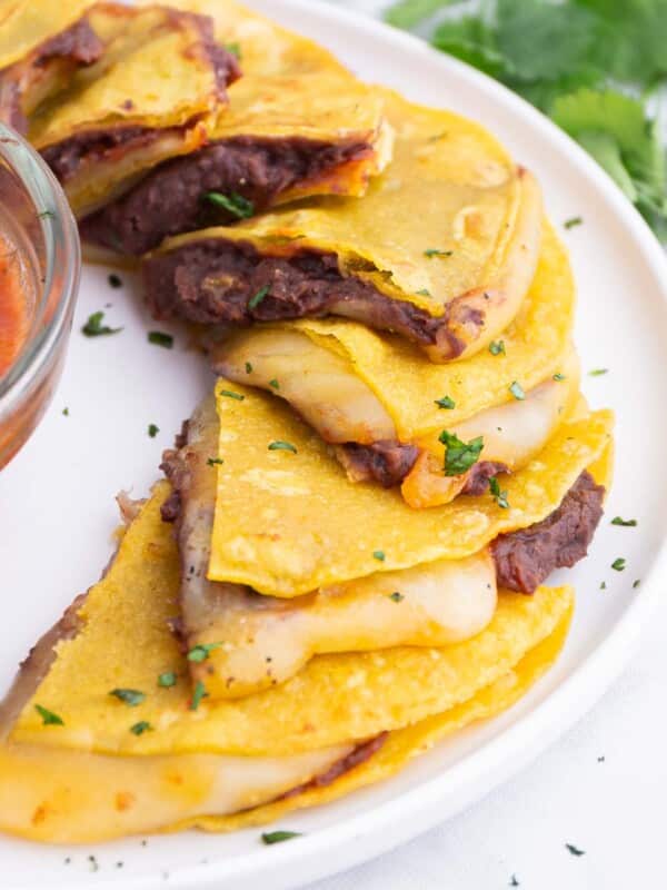 A tray of corn tortilla quesadillas are served on a tray with salsa.