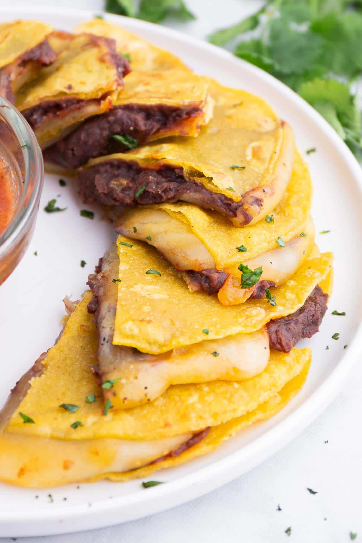 A tray of corn tortilla quesadillas are served on a tray with salsa.