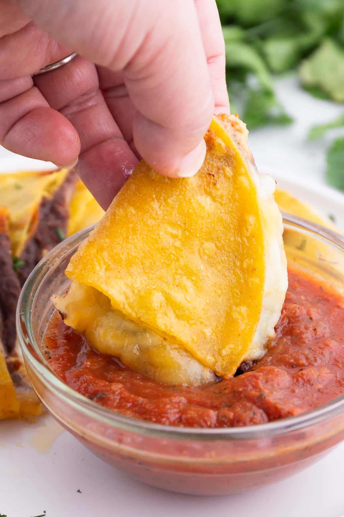 A hand dips a corn tortilla quesadilla in salsa.