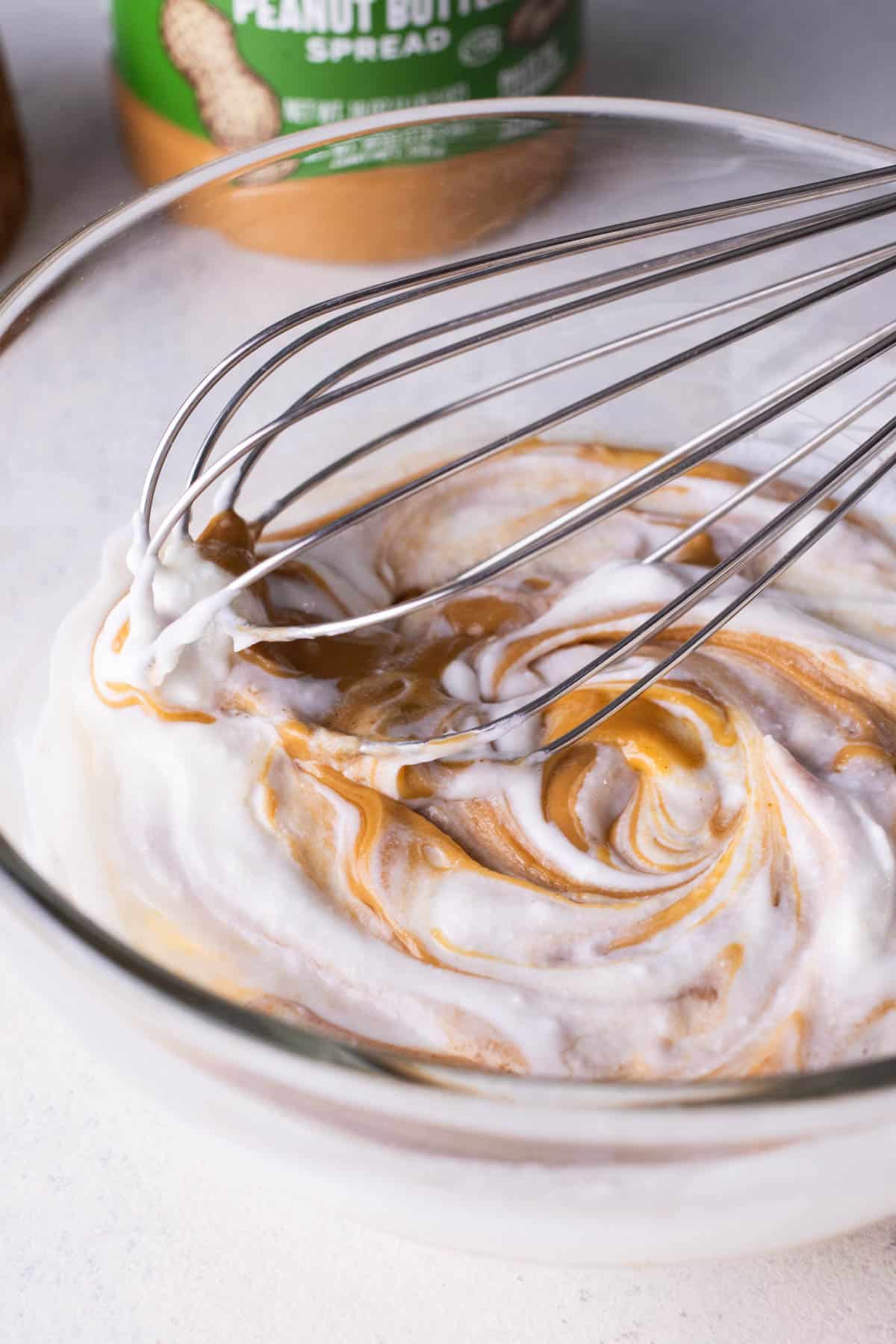 Greek yogurt and peanut butter are whisked together in a glass bowl.