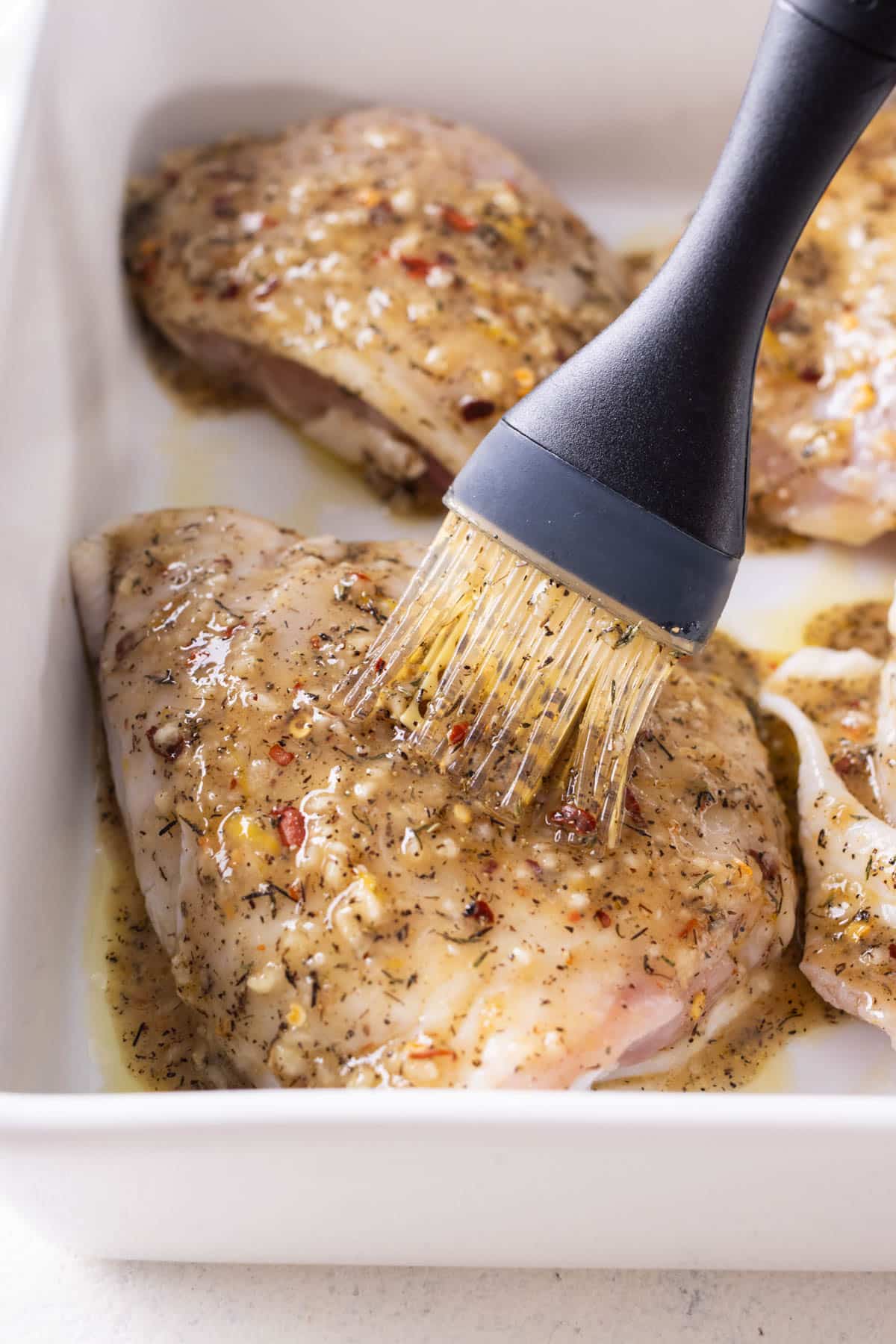 Seasoning is brushed onto chicken thighs.