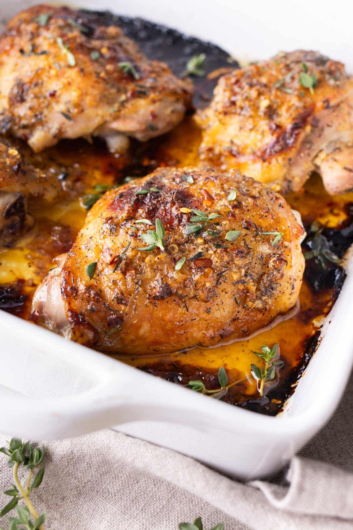 Chicken thighs seasoned with a honey mustard glaze are baked in a white dish.