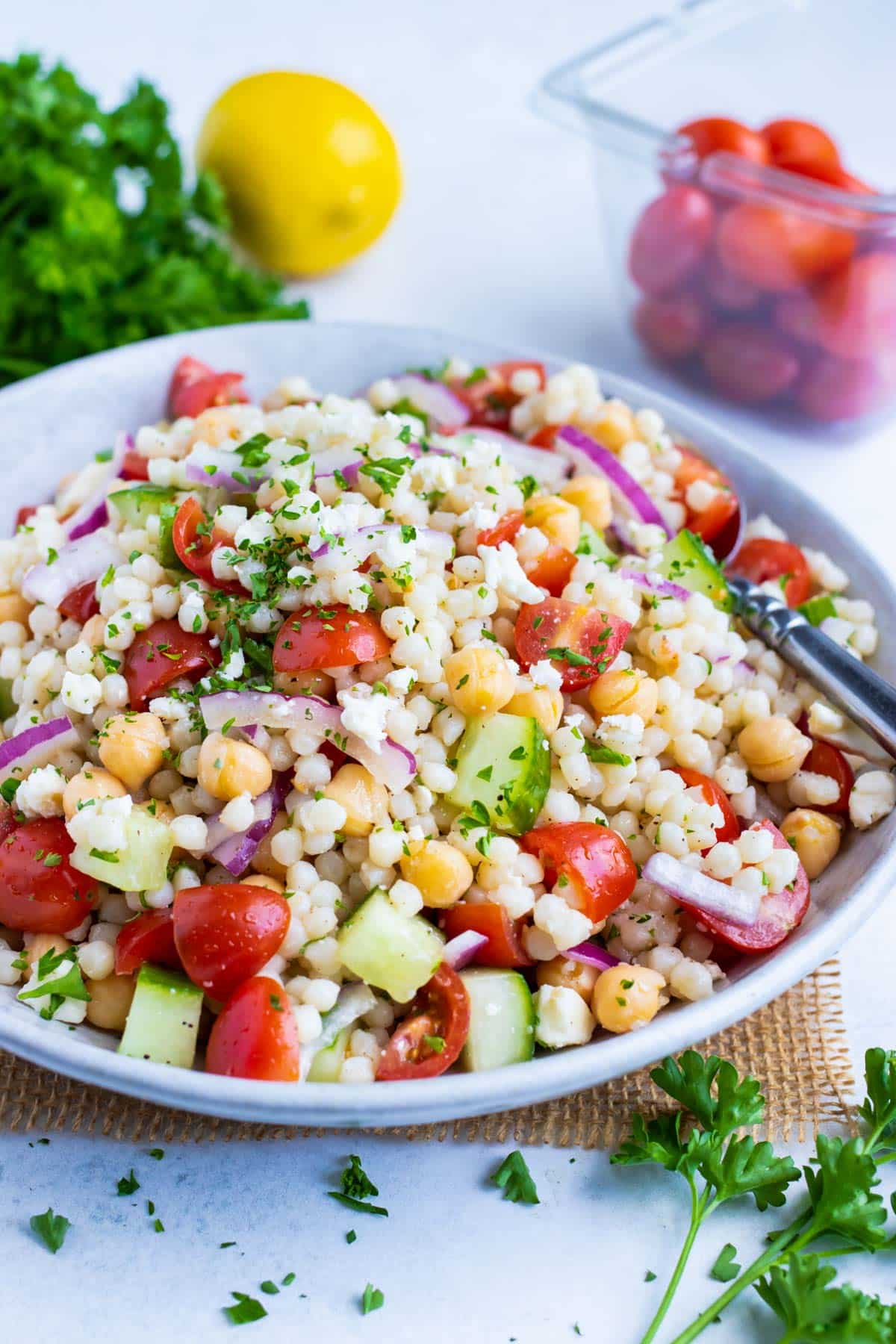 A big glass bowl full of a Mediterranean Couscous Salad with tomatoes, feta, garbanzo beans, and cucumbers.
