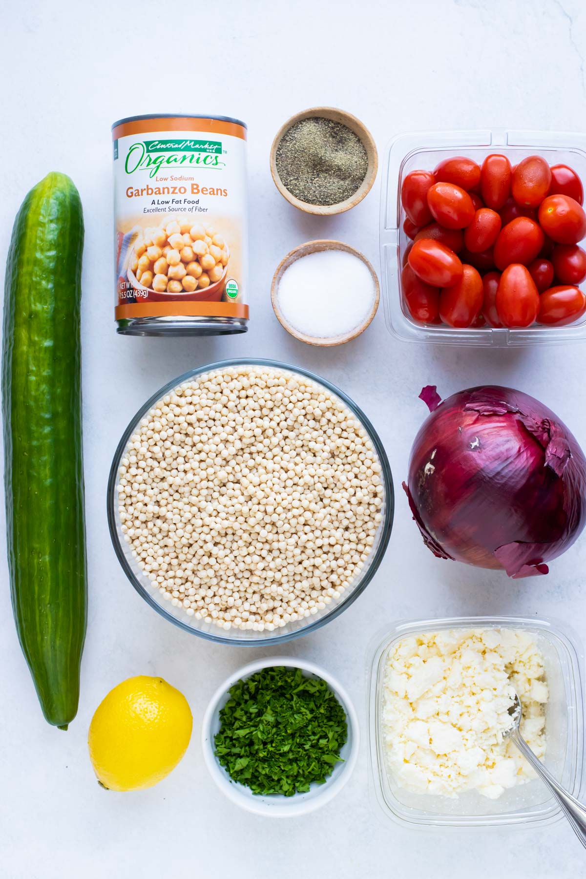 Cucumber, garbanzo beans, couscous, tomatoes, onion, feta, parsley, and lemon as ingredients for a recipe.