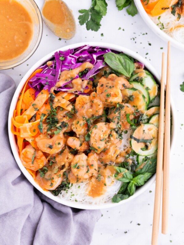 A spring roll in a bowl is served with chop sticks.