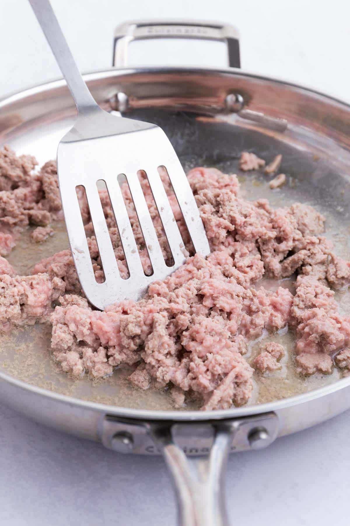 A spatula stirs ground turkey as it cooks in a skillet.