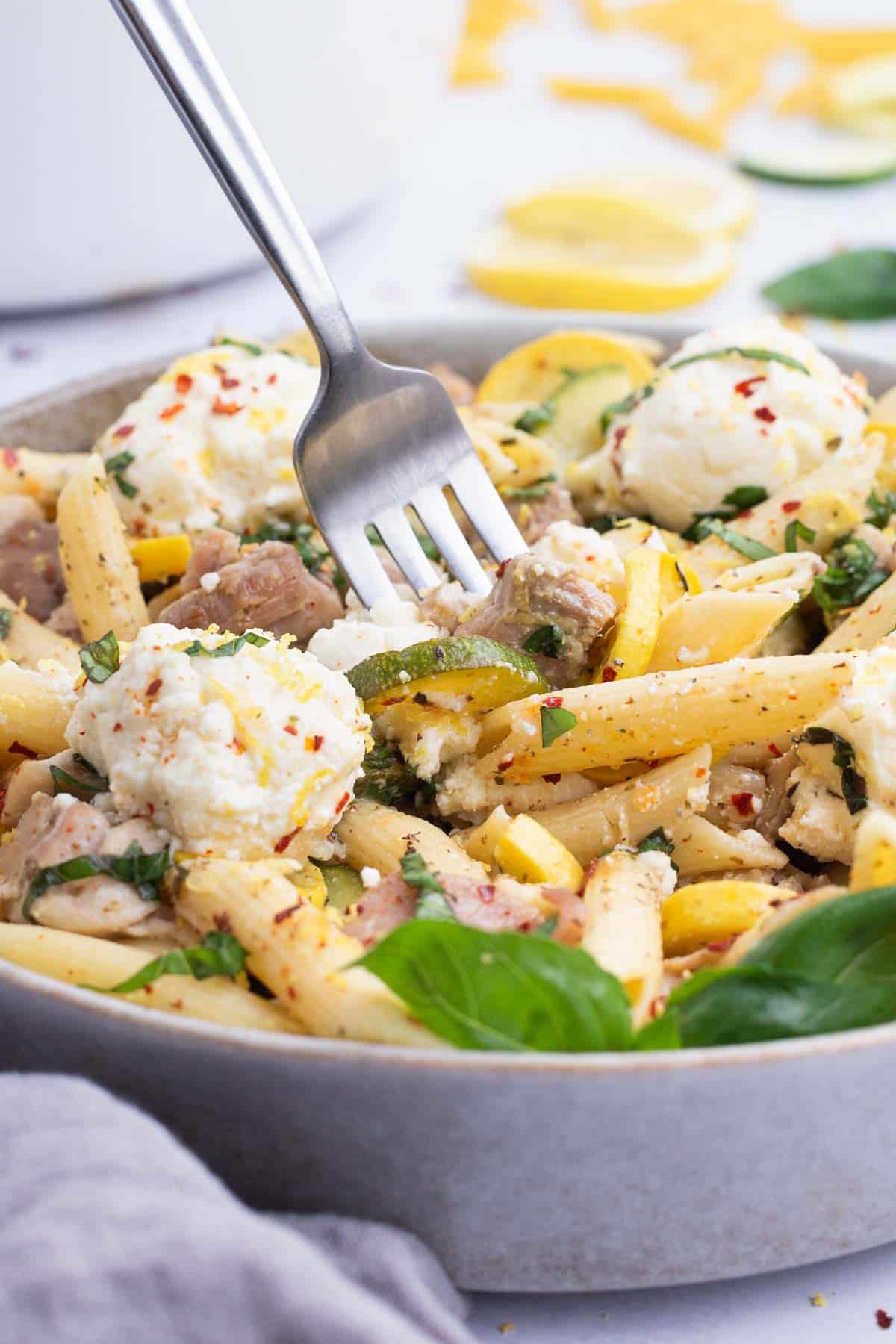 A fork digs into a bowl filled with lemon ricotta pasta with chicken.
