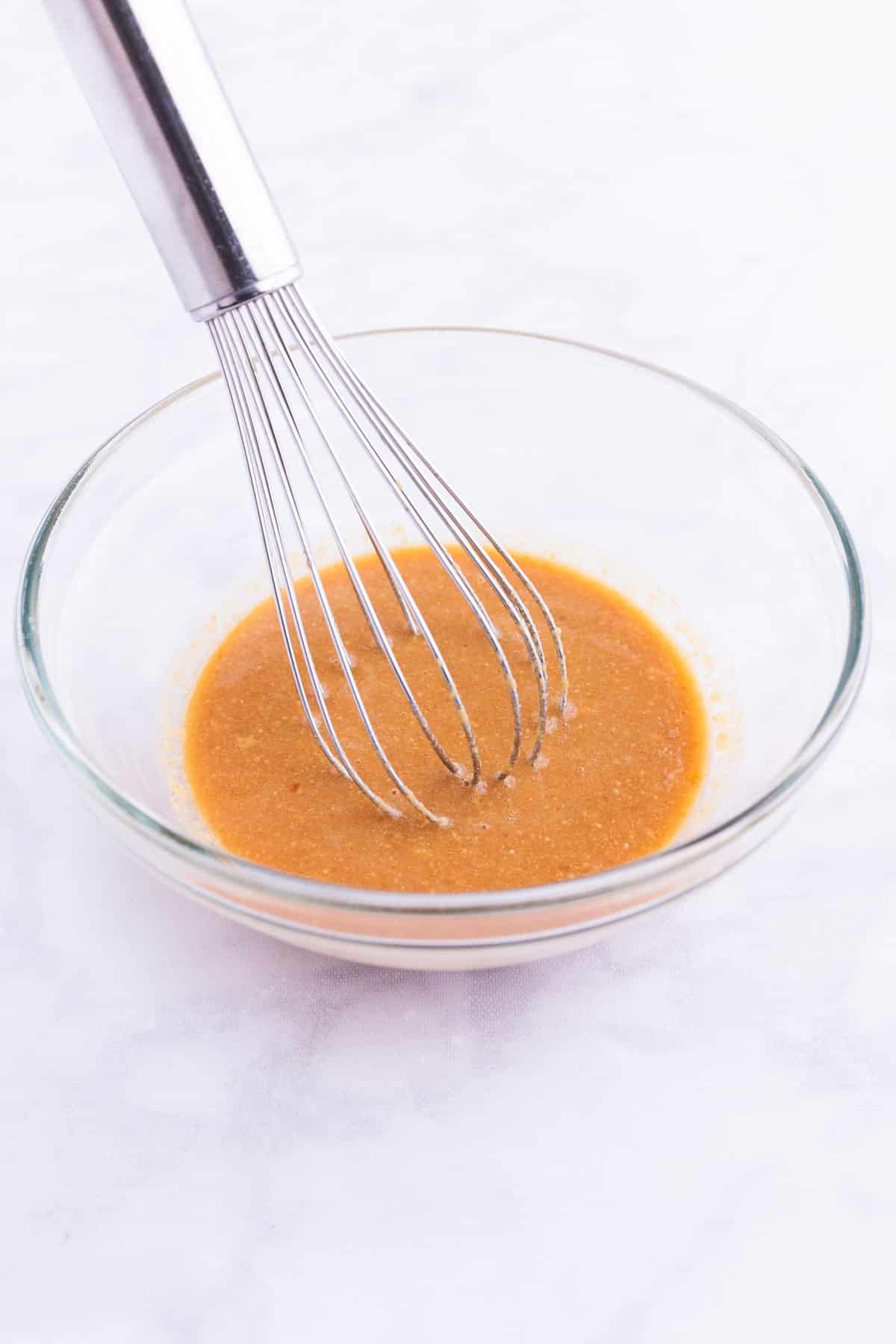 Peanut sauce is whisked together in a glass bowl.