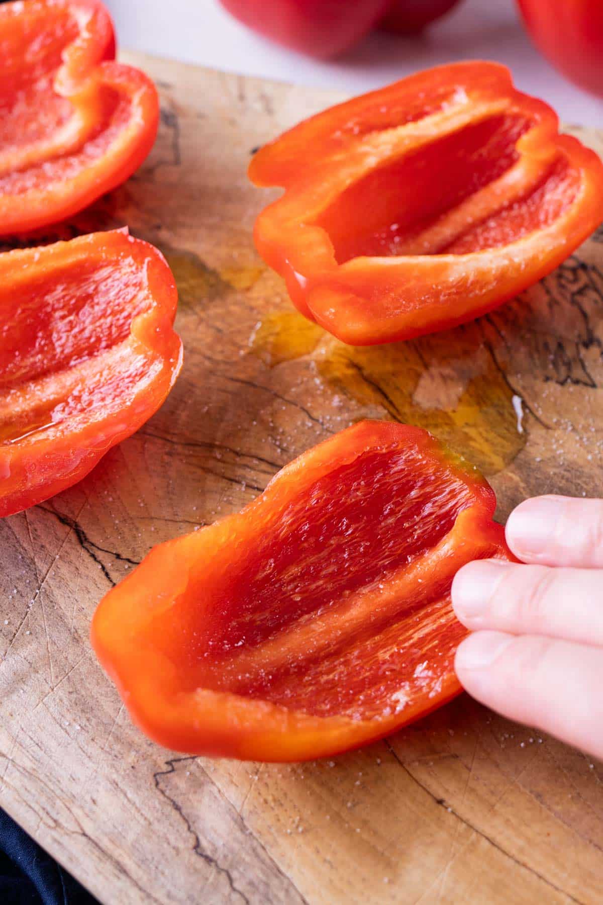 A hand rubs olive oil and salt into sliced bell peppers.