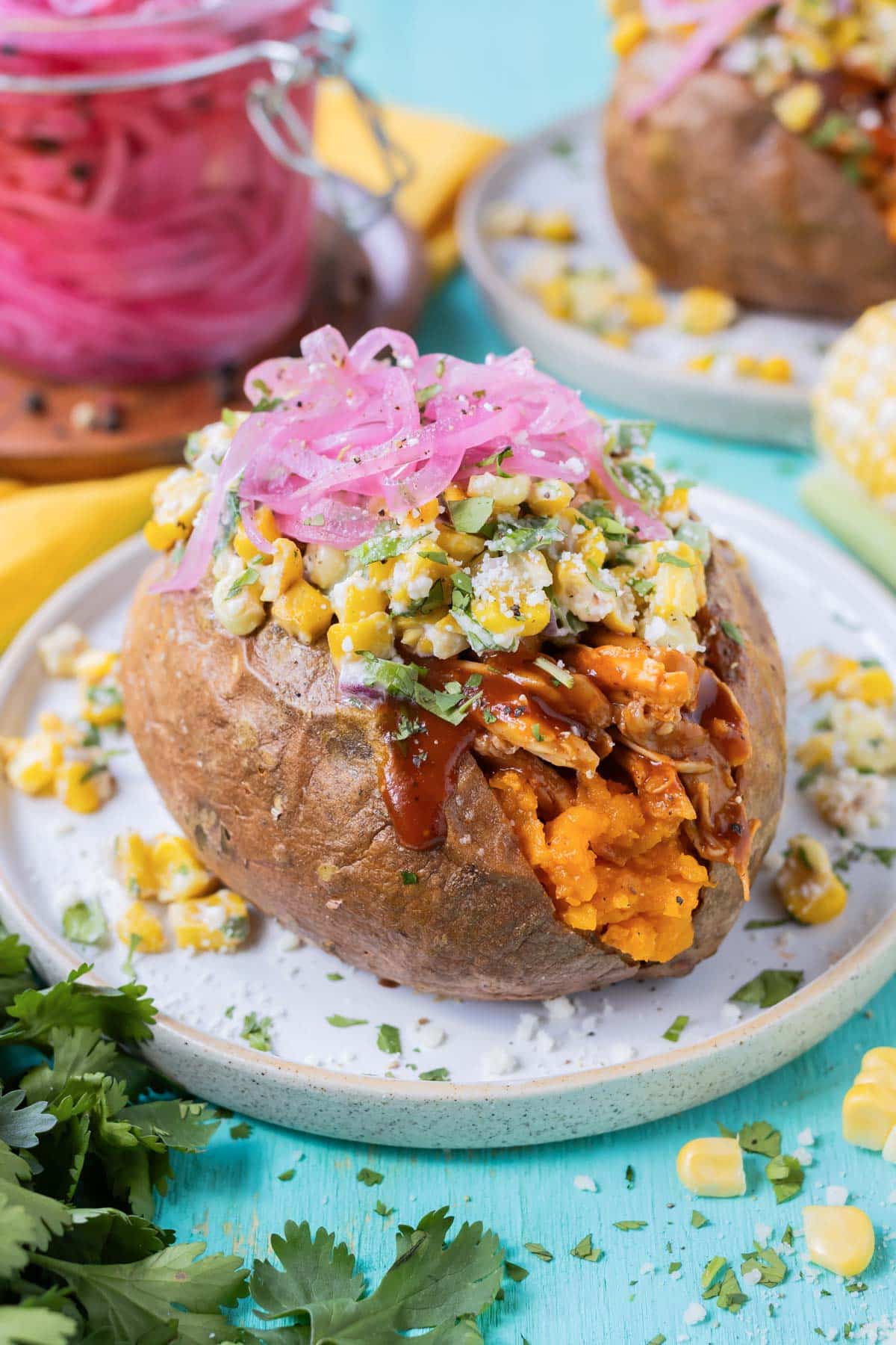 A baked sweet potato that is stuffed with barbecue chicken and topped with corn.