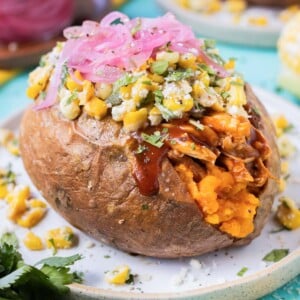 BBQ chicken stuffed sweet potatoes are served with Mexican street corn salad and pickled red oinons.