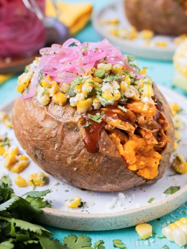 BBQ chicken stuffed sweet potatoes are served with Mexican street corn salad and pickled red oinons.