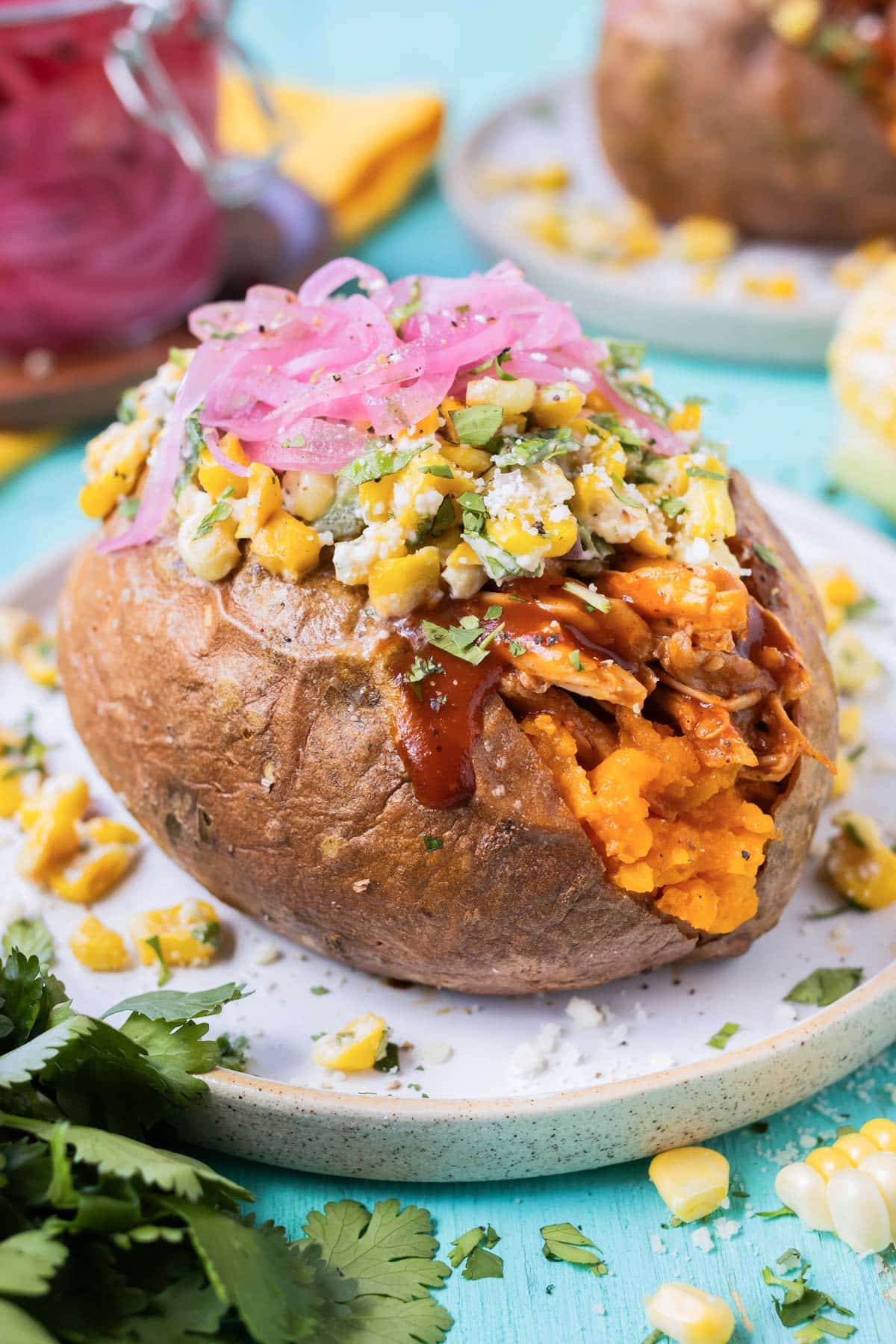 BBQ chicken stuffed sweet potatoes are served with Mexican street corn salad and pickled red oinons.