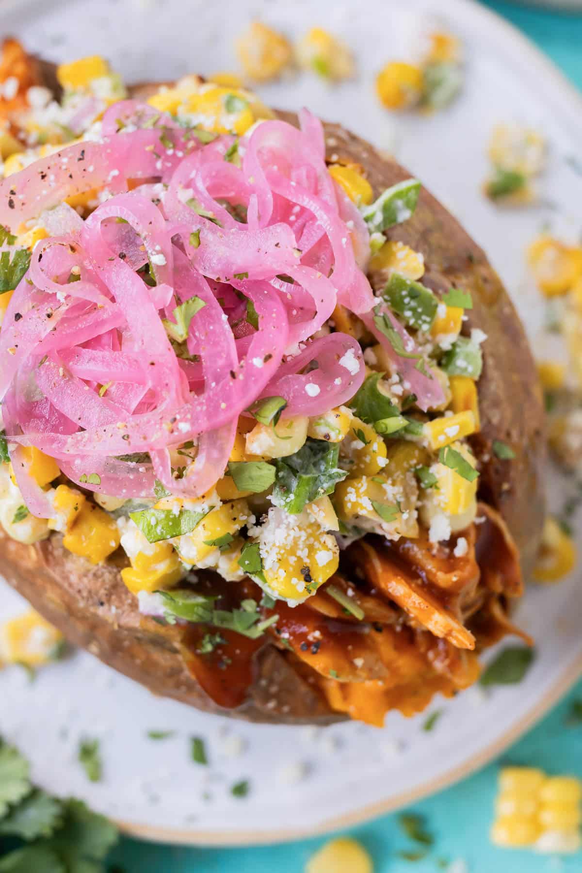 BBQ chicken stuffed sweet potatoes are served with Mexican street corn salad and pickled red oinons.