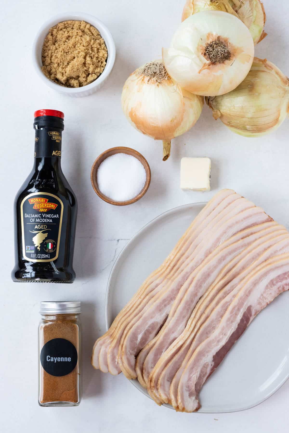 Bacon, onion, balsamic vinegar, brown sugar, and salt are on a table to make a bacon onion jam recipe.