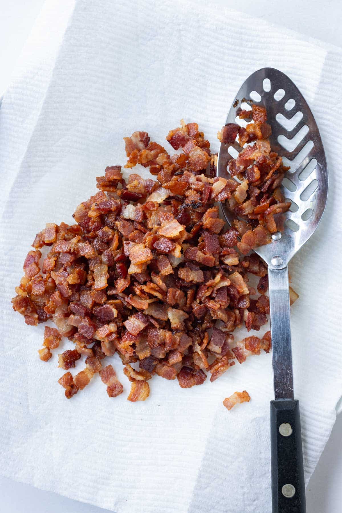 Cooked bacon is drained on a plate with paper towels.