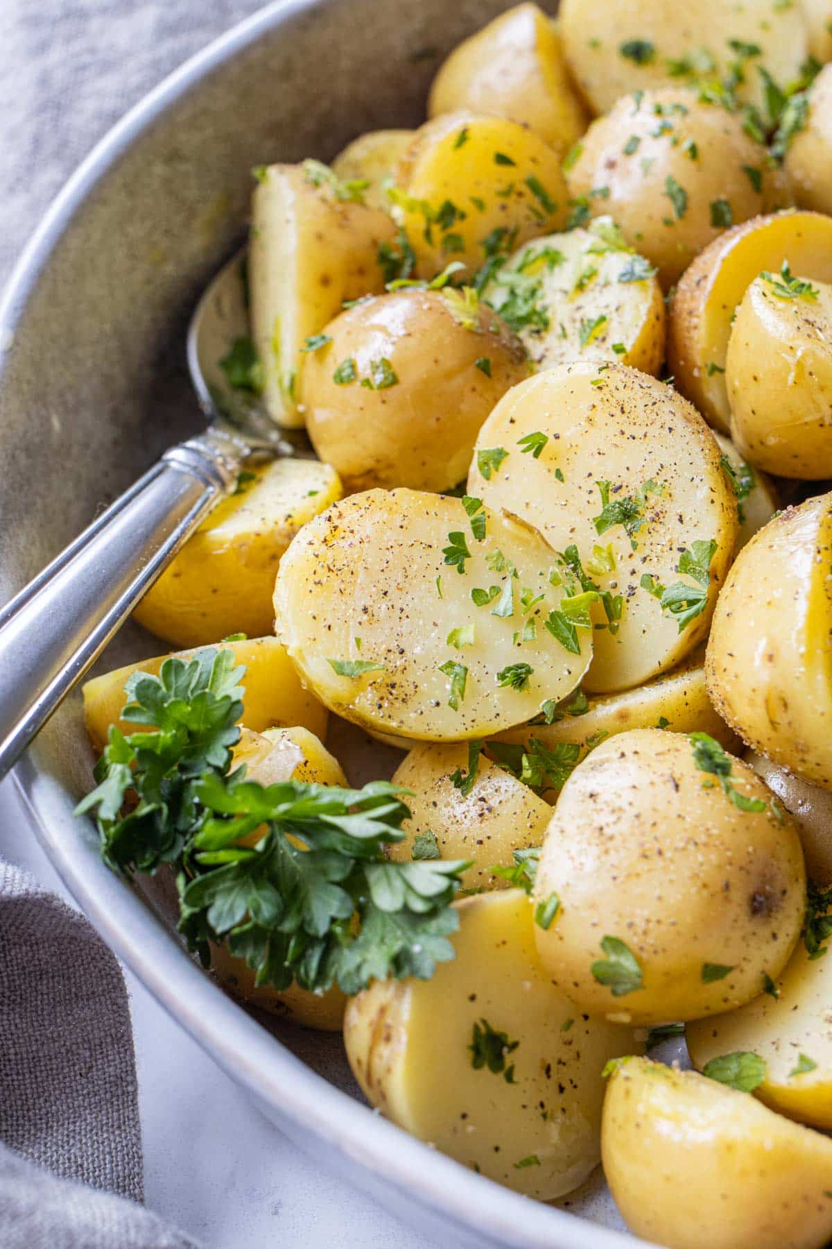 A spoon serving up boiled potatoes from a grey bowl.