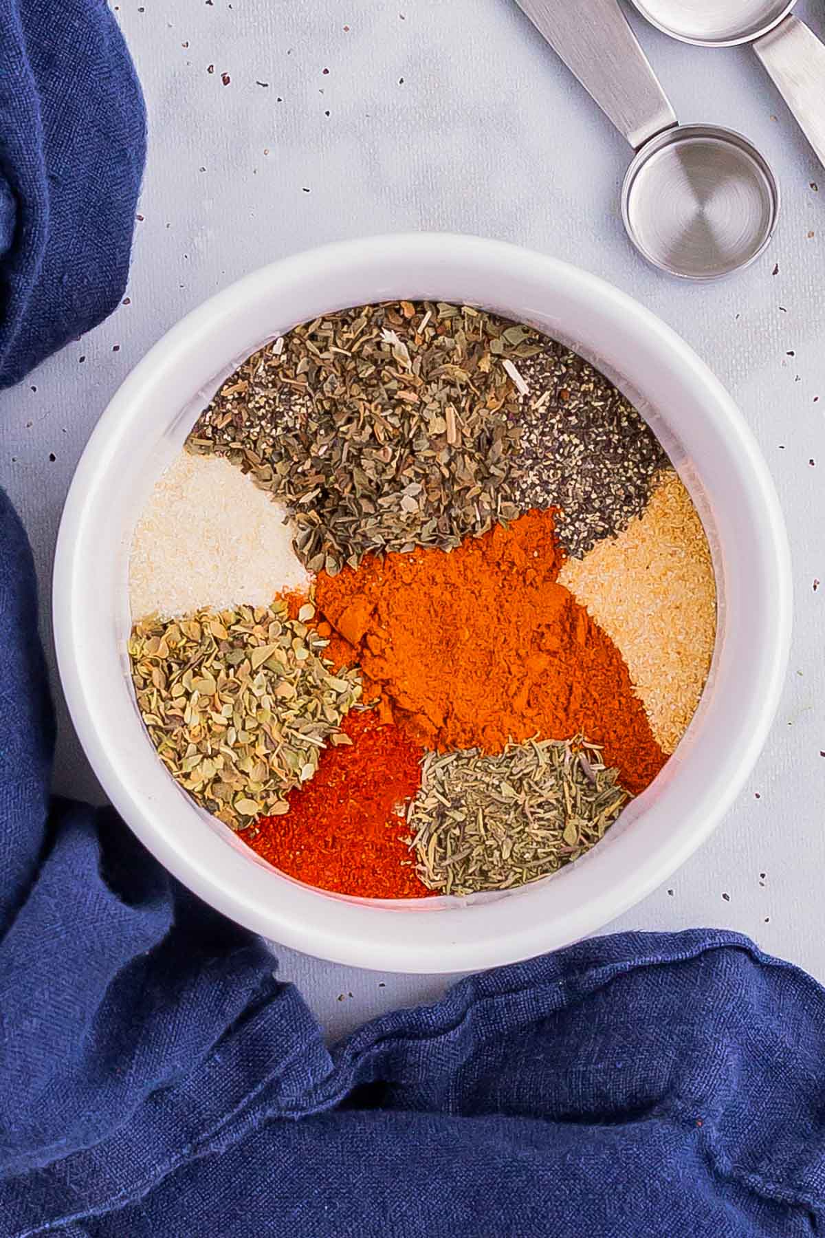 Spices, dried herbs, garlic and onion powder in a white bowl for a homemade Cajun seasoning recipe.