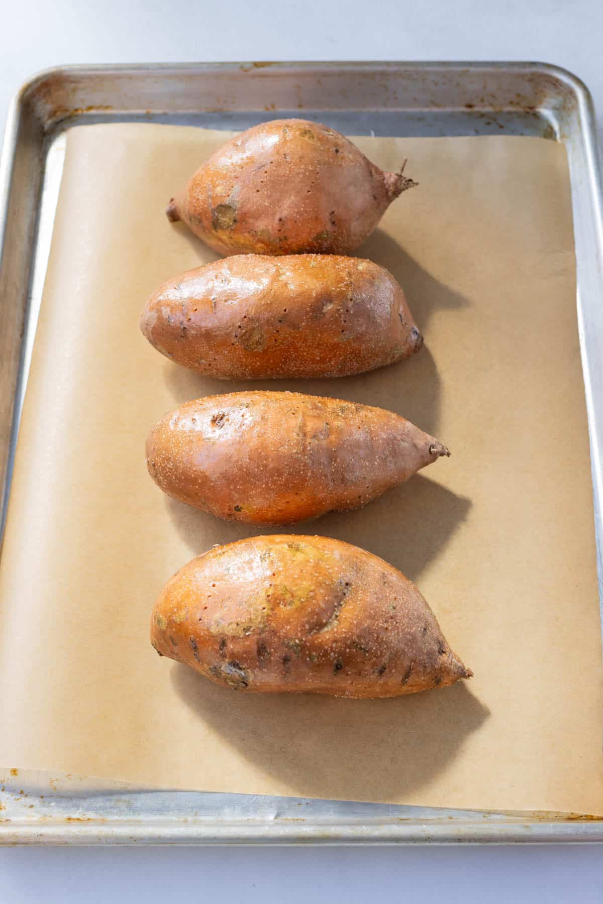 Sweet potatoes that have been covered in oil, salt, and black pepper and are placed on a sheet pan to bake in the oven.