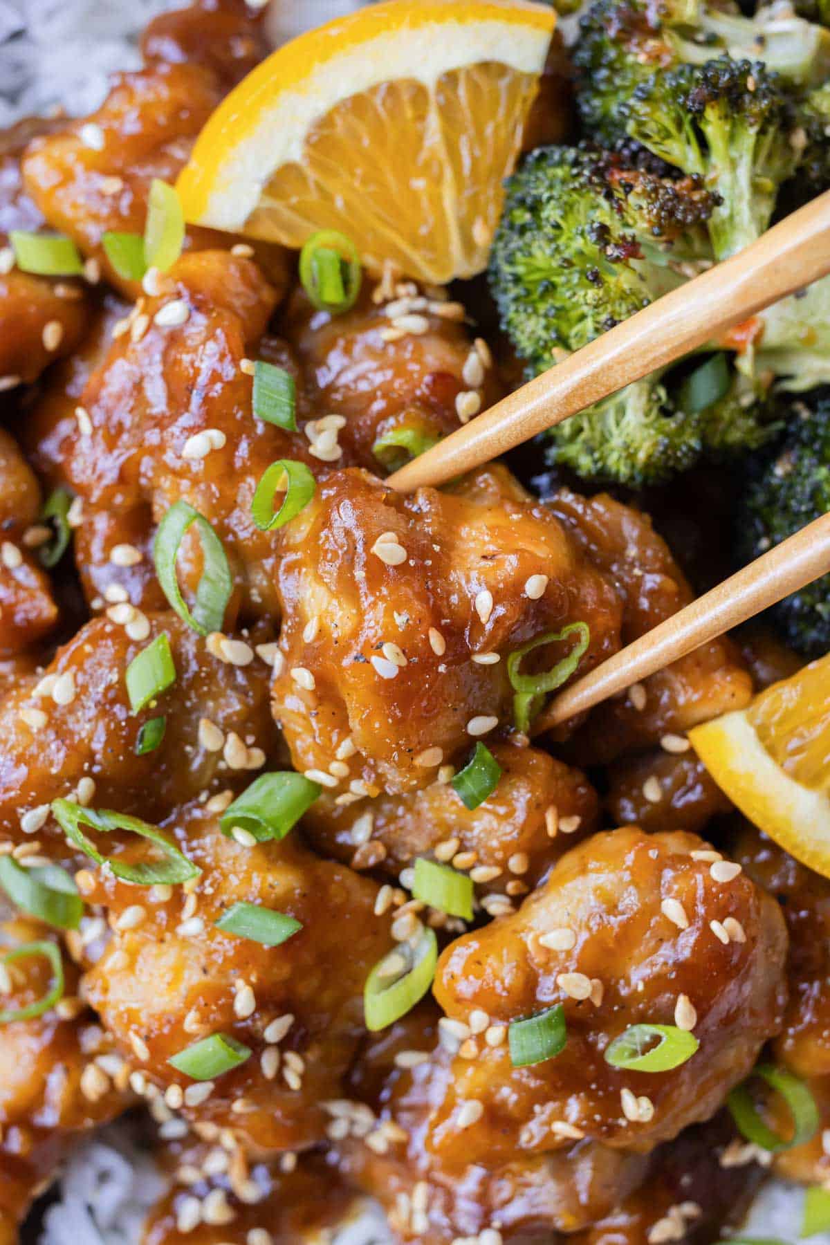 Chopsticks are picking up a single piece of homemade orange chicken from a bowl.