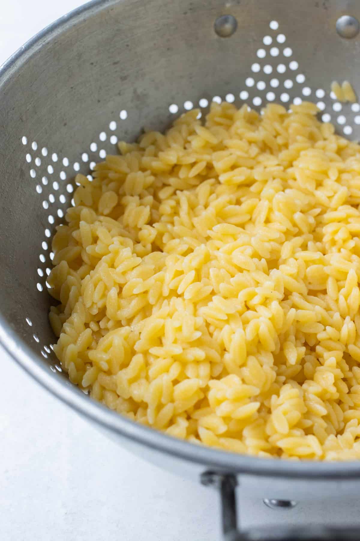 Cooked orzo is drained in a colander.