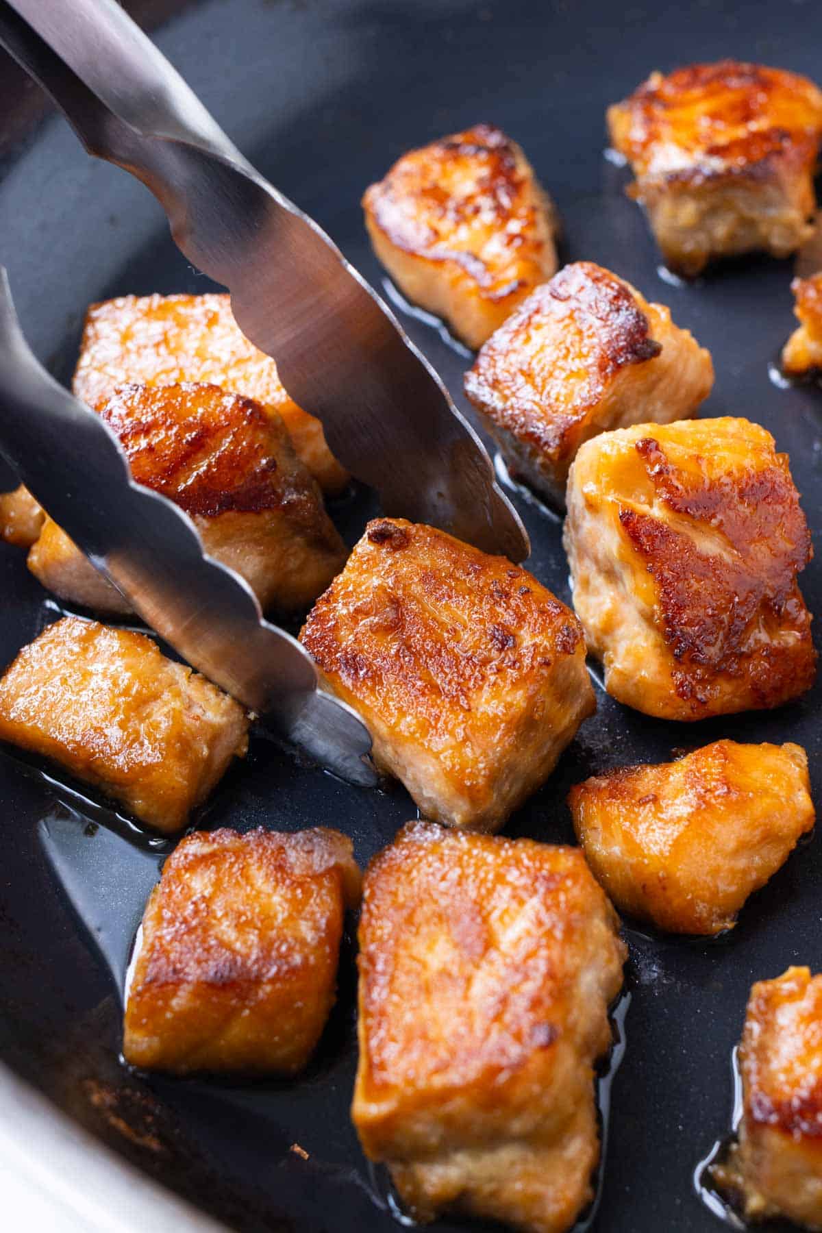 Marinated teriyaki salmon bites are cooked in a skillet.