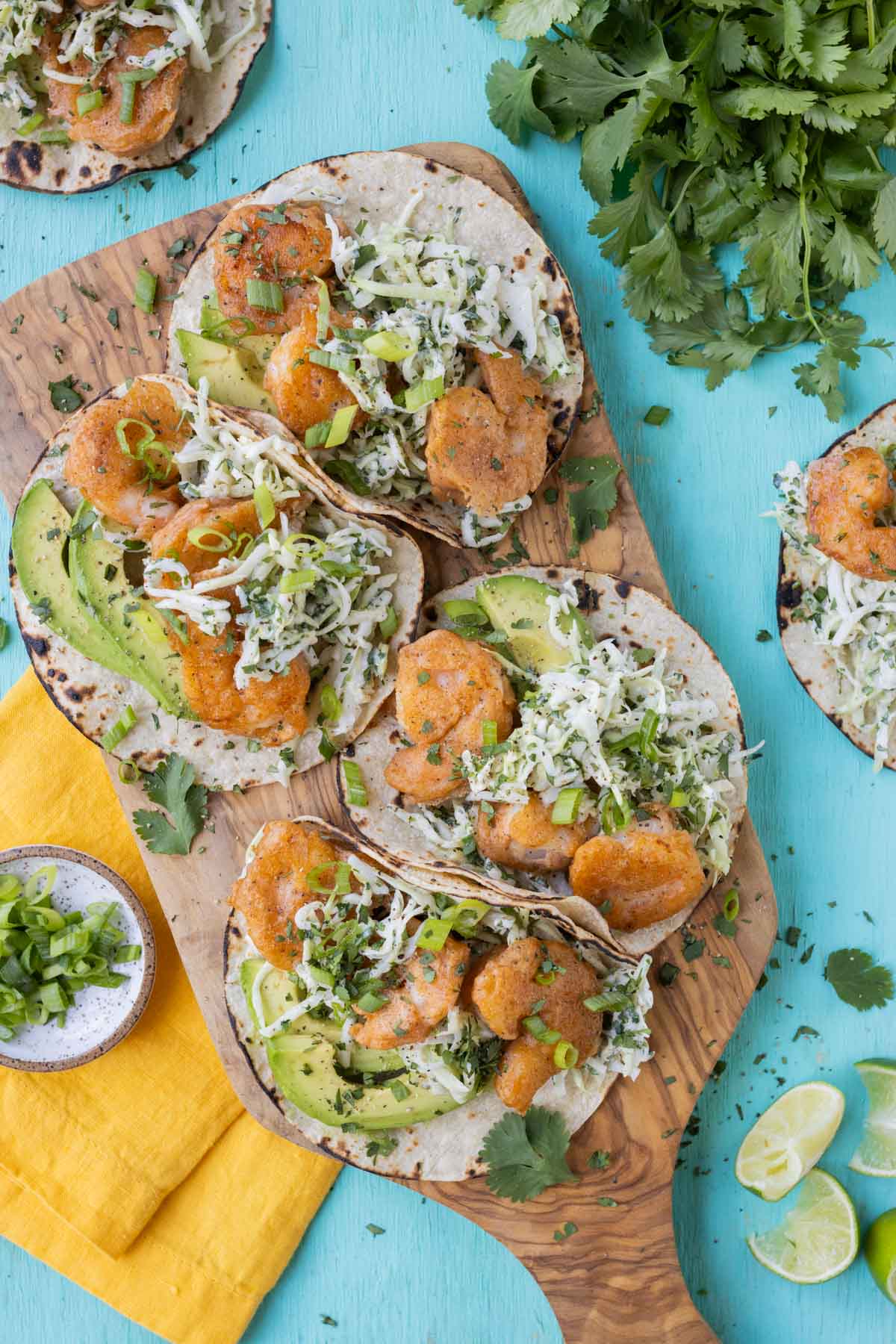 A wood board full of Baja shrimp tacos are ready to serve on a turquoise table.