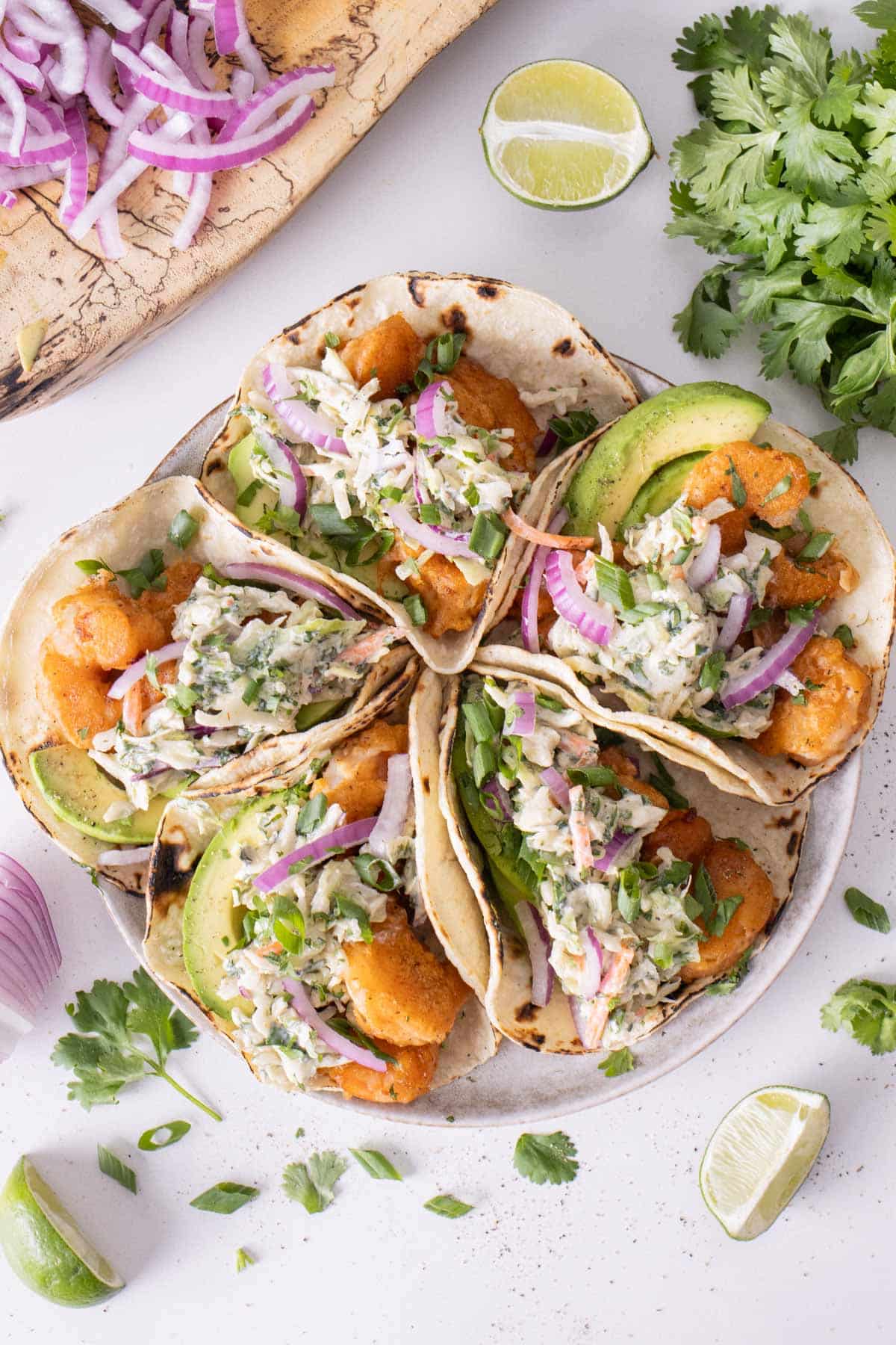 A plate of Baja shrimp tacos with cilantro, limes, and red onion.
