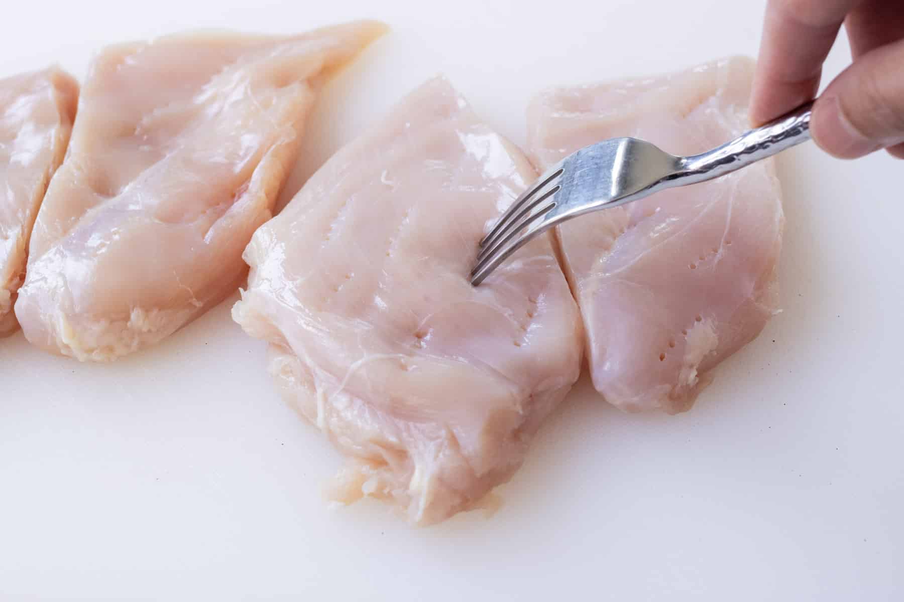 Chicken breasts are poked with a fork.