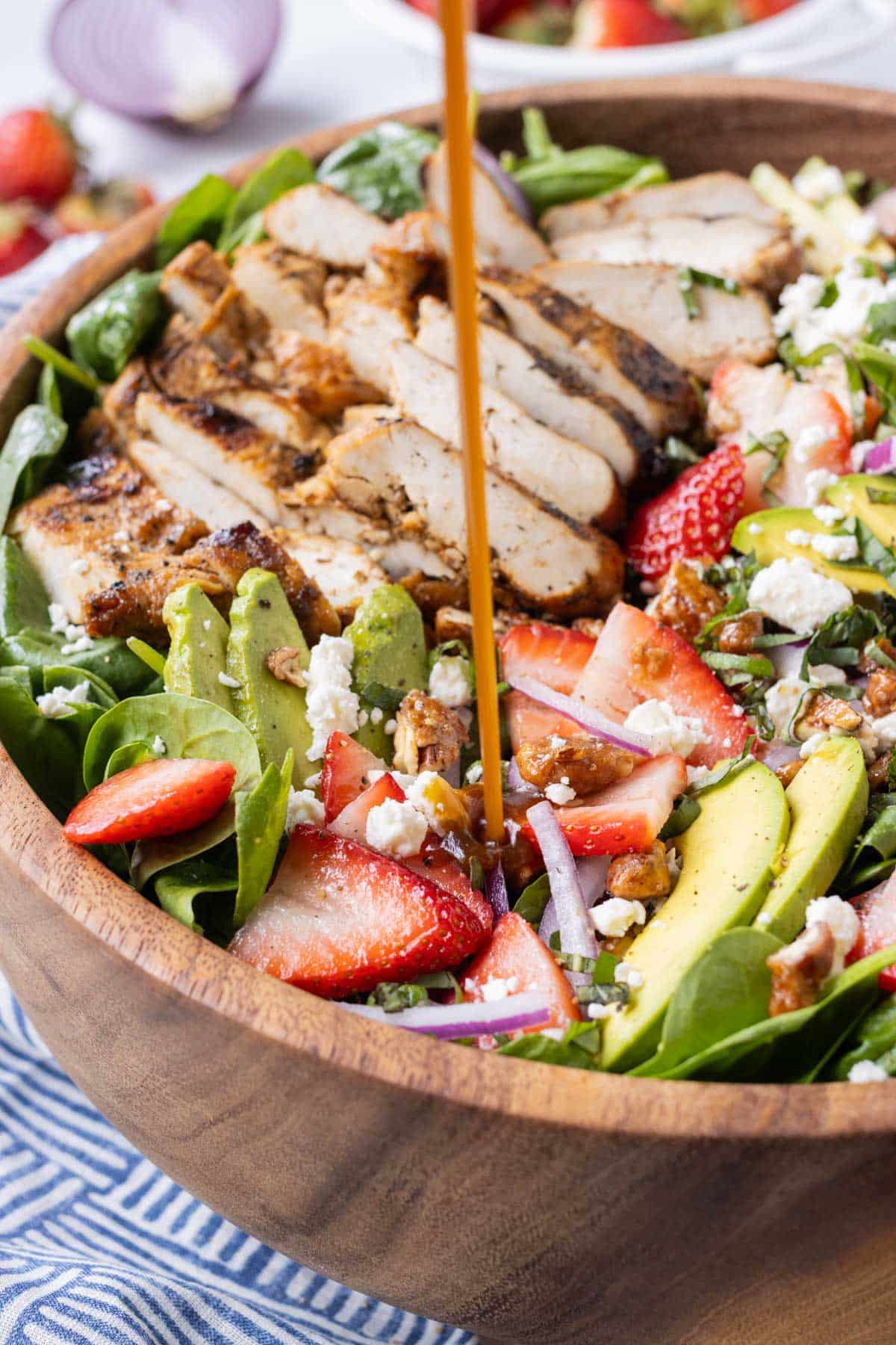 Balsamic dressing is poured over a strawberry spinach salad with grilled chicken.