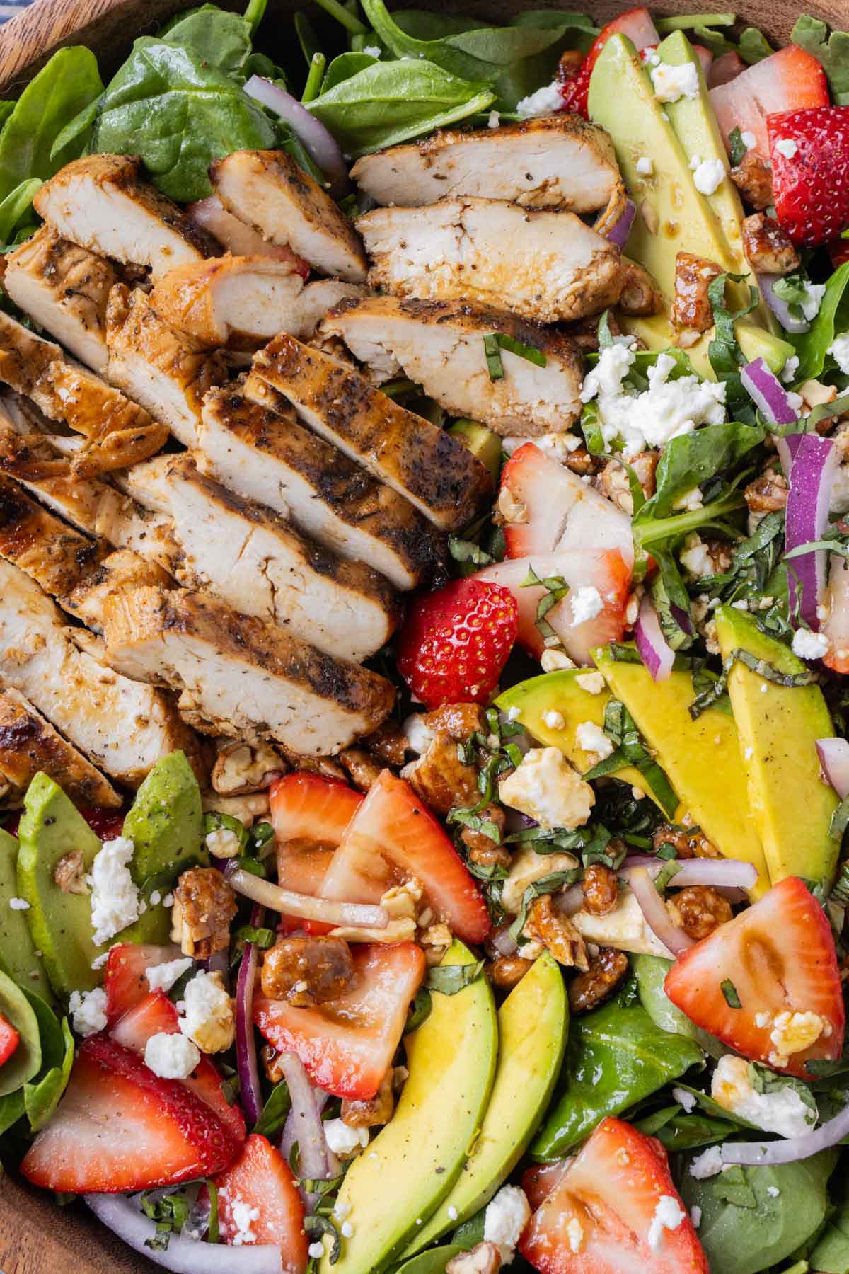 Grilled chicken is added on top of a spinach salad with strawberries and a balsamic vinaigrette.