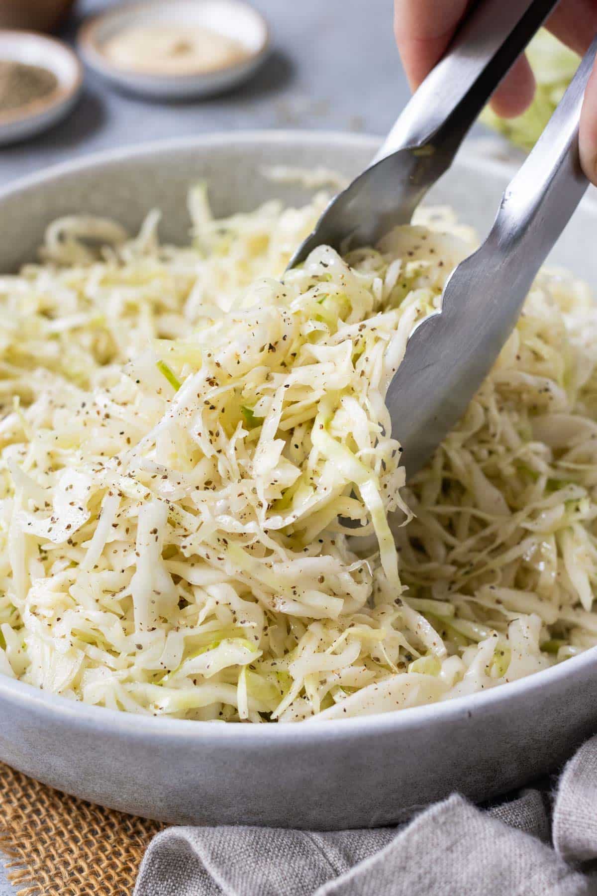 Tongs are used to stir and serve apple cider slaw.