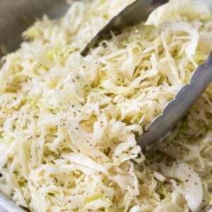 Tongs are used to stir and serve apple cider slaw.