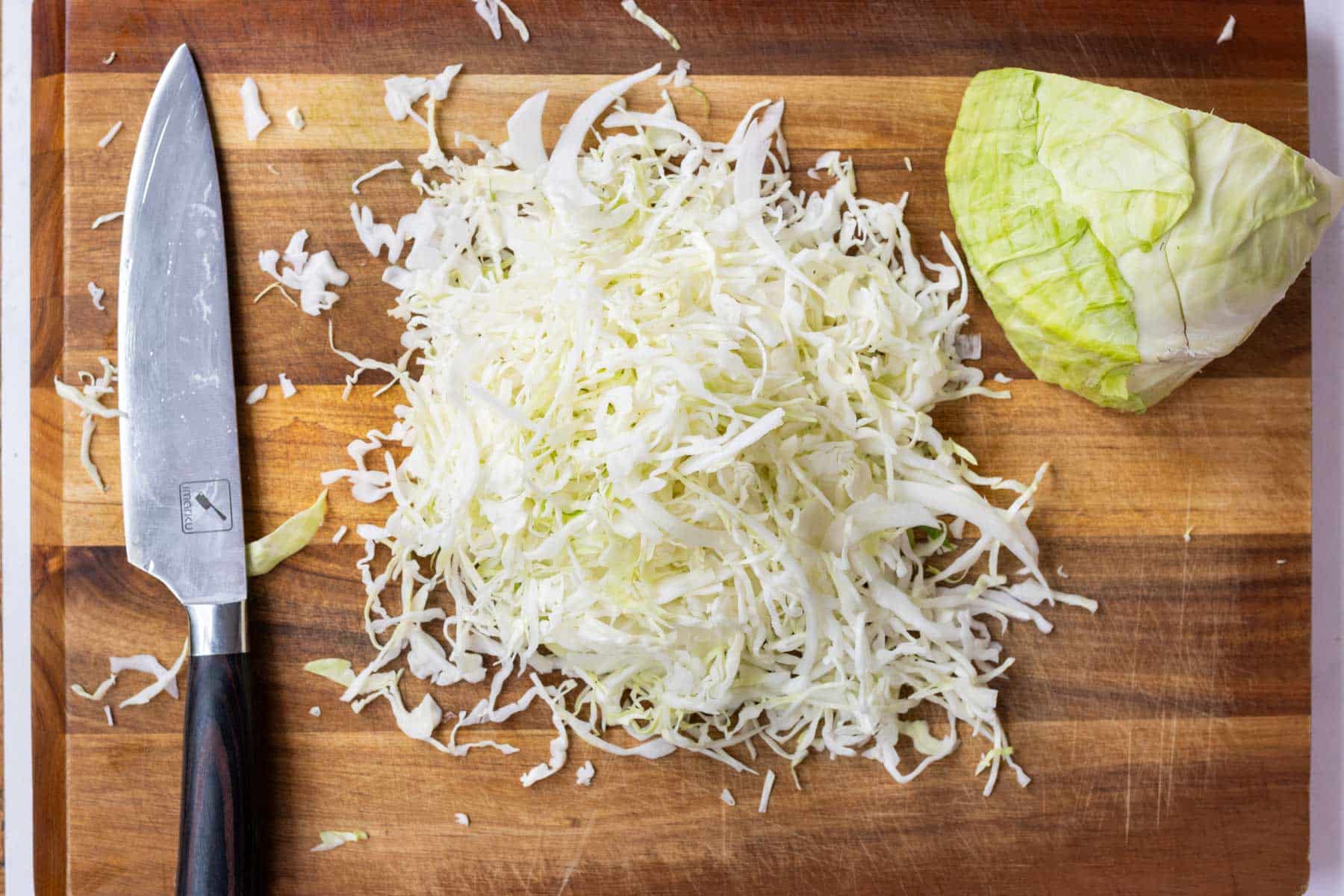 A head of green cabbage is shredded on a cutting board.